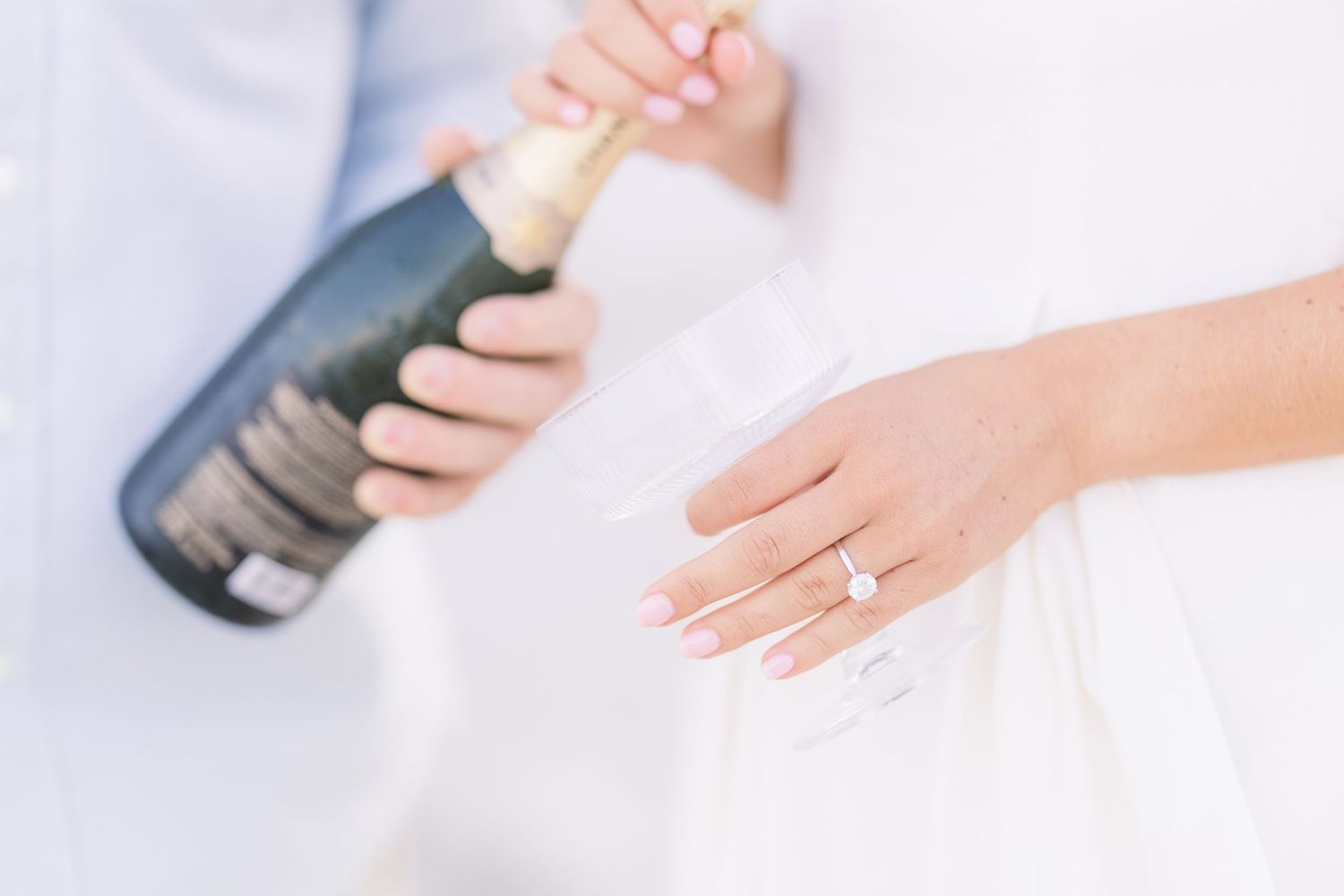 Close-up of hands with engagement ring against white background.