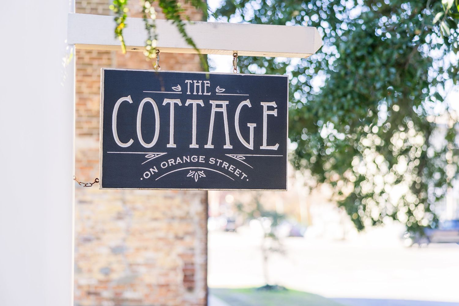A rustic chalkboard sign reading 'The Cottage' mounted on a brick wall.