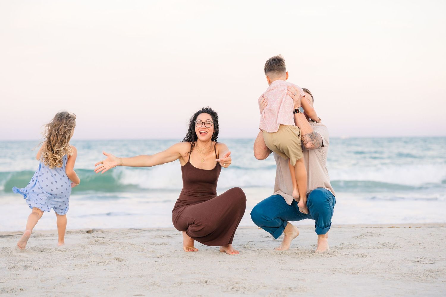 Family of four enjoying a fun beach day at sunset, with parents playing with young children on sandy shore near ocean waves.