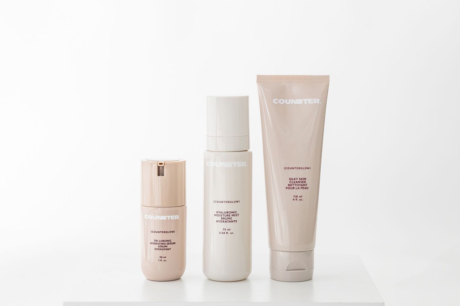 Three beige cosmetic bottles lined up on white background showing product packaging design.