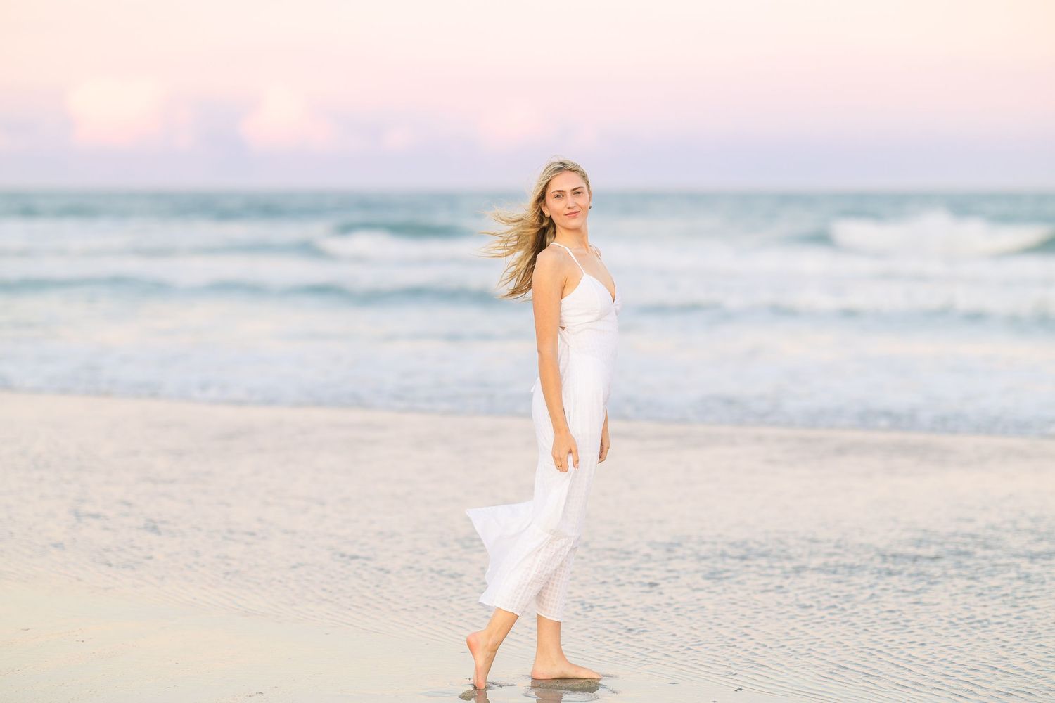 Dreamy beach portrait with flowing white dress against ocean waves.