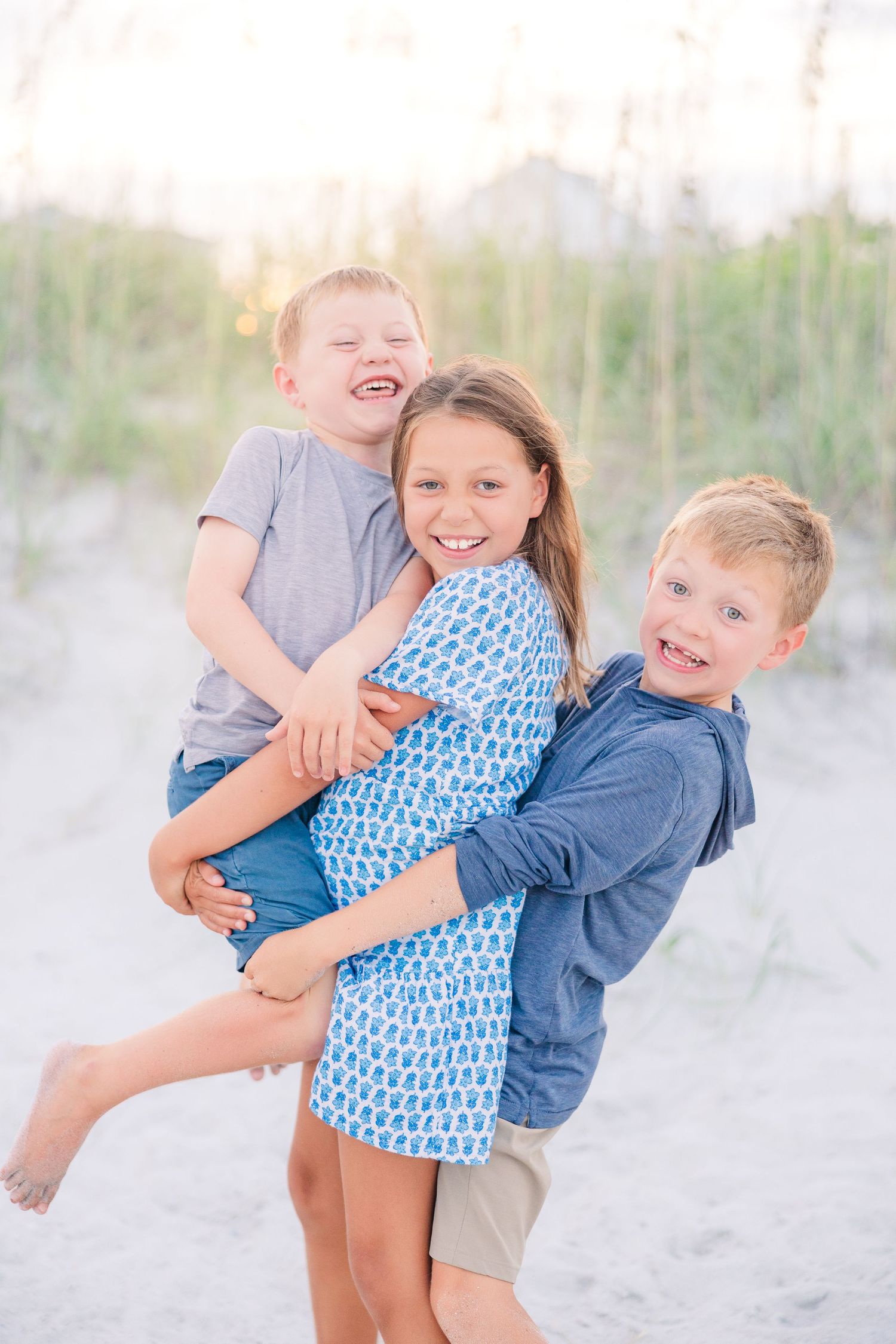 Three children playing and laughing together on a beach during a sunset photoshoot.