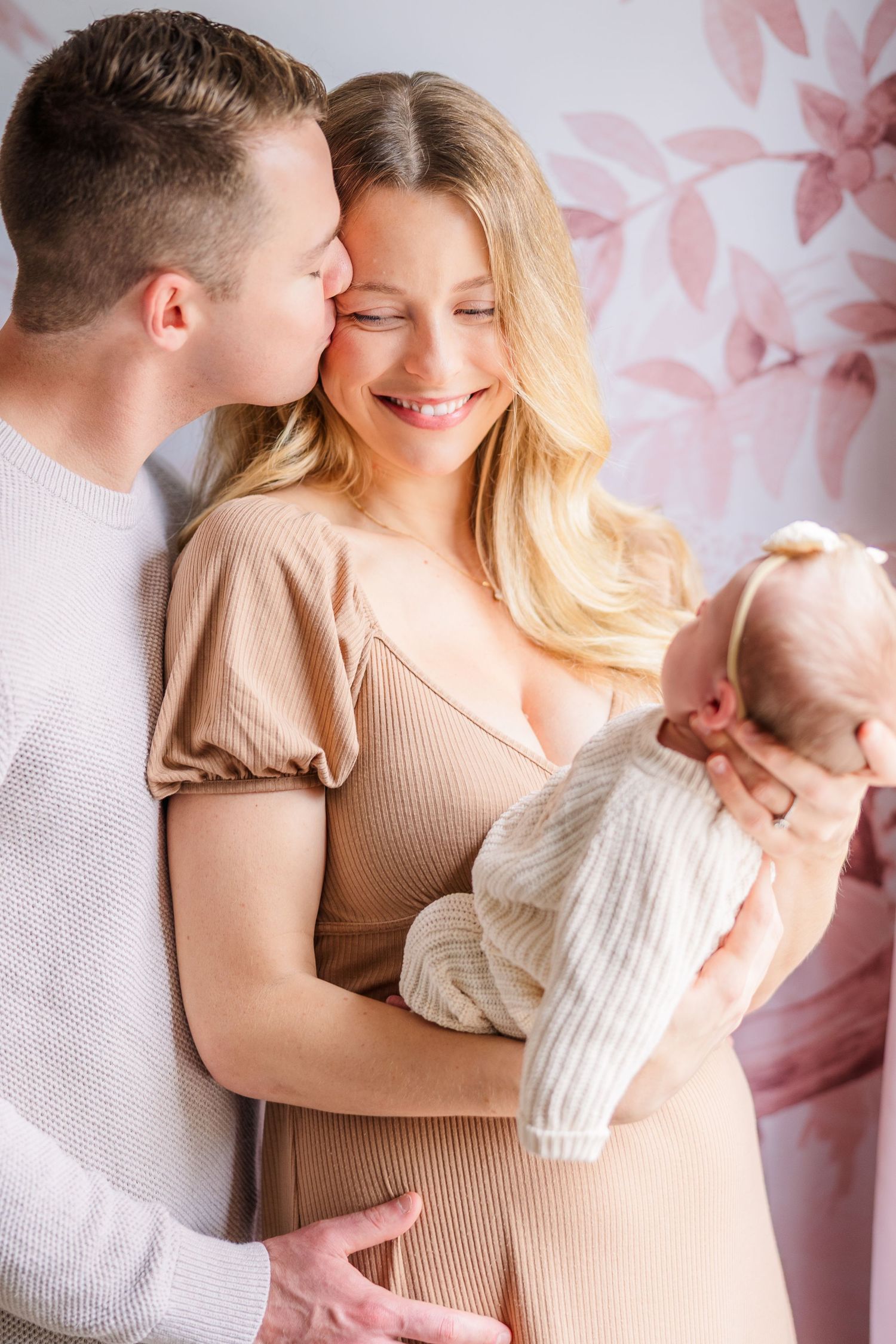 Loving family portrait series with neutral tones against a pink floral wallpaper.