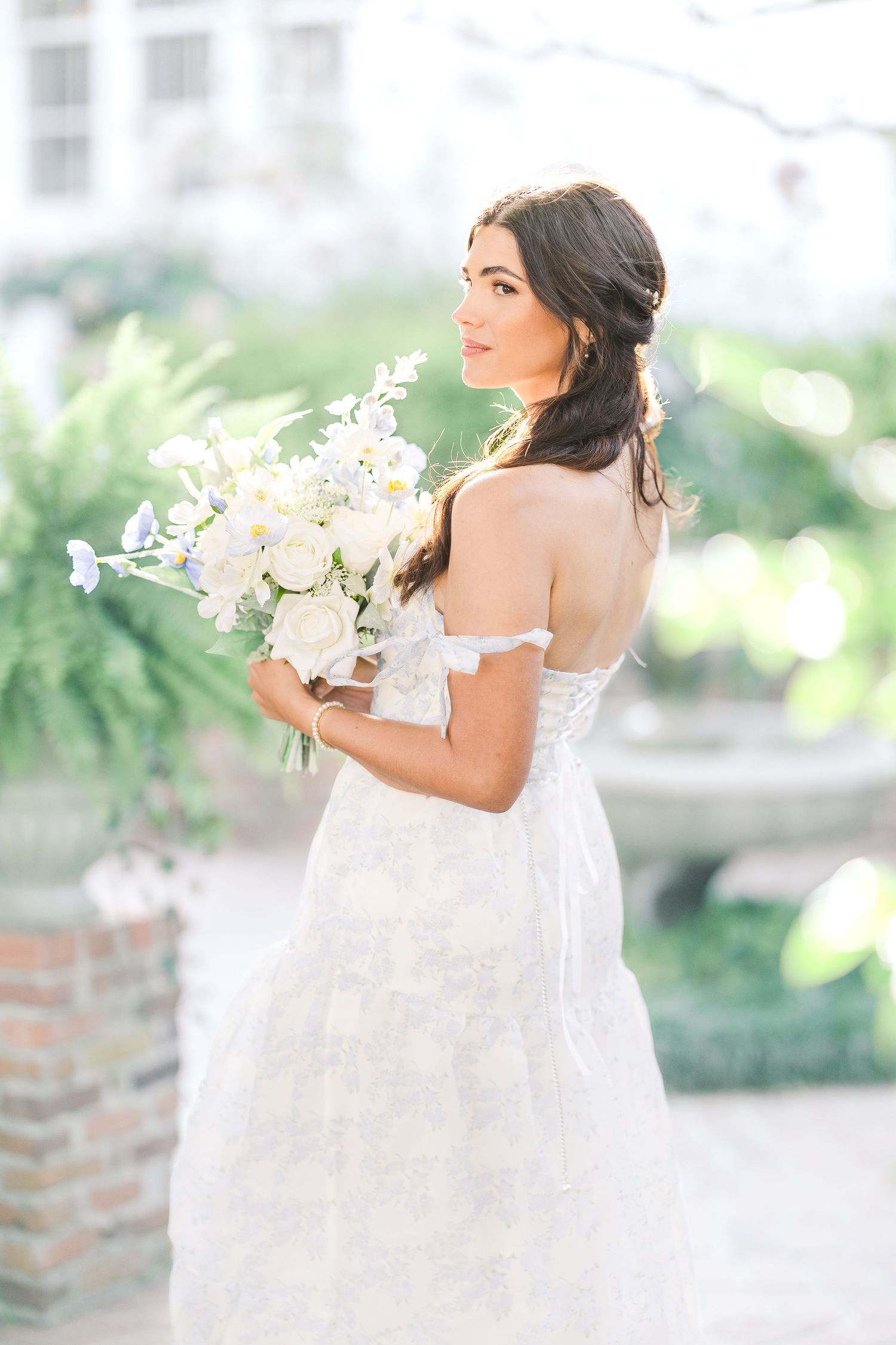 Elegant bride in white lace gown holds a bouquet of white orchids against a bright outdoor backdrop sycamore bend wilmington nc wedding