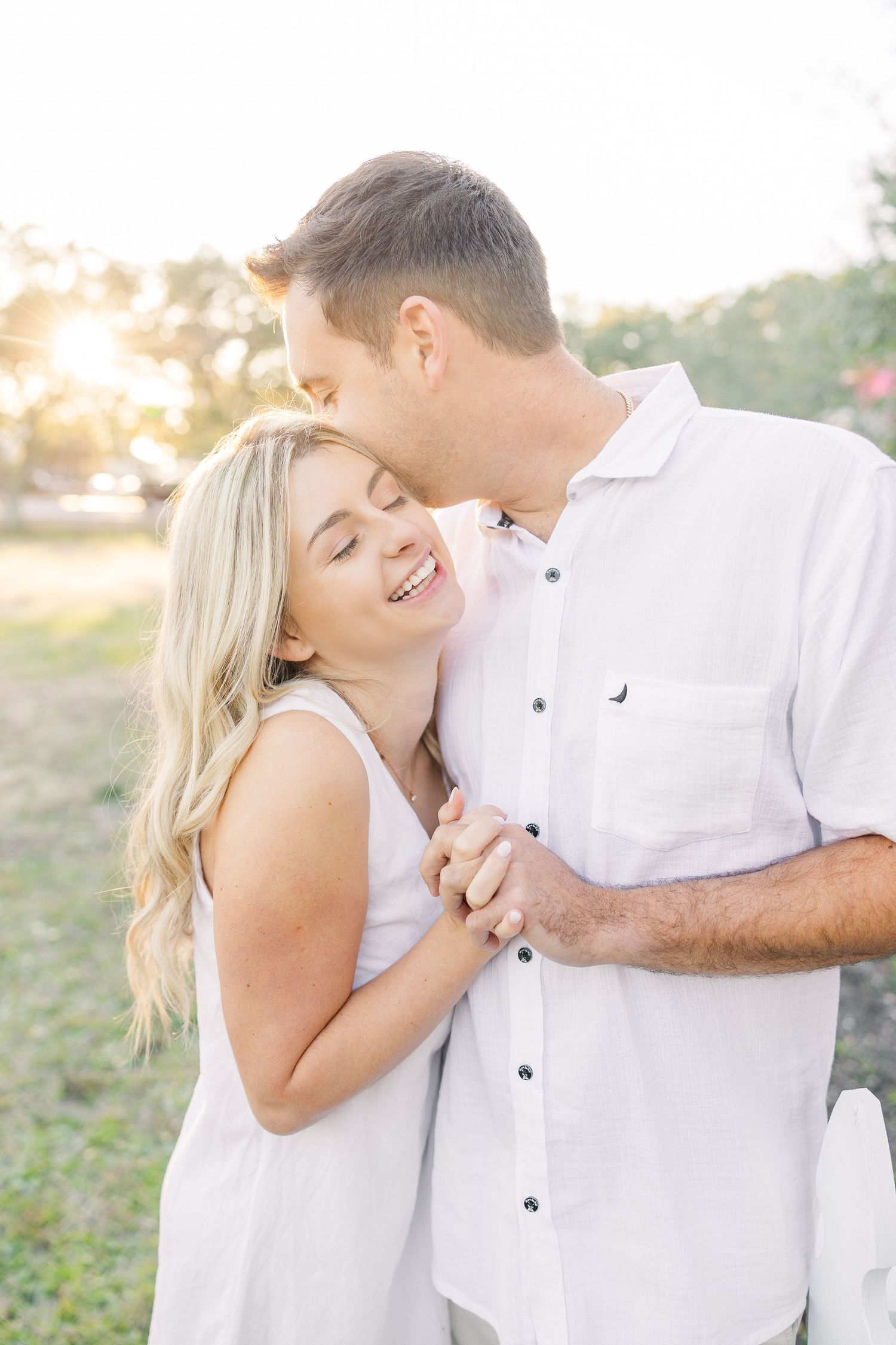 Couple in white clothing sharing playful and romantic moments in a natural outdoor setting.