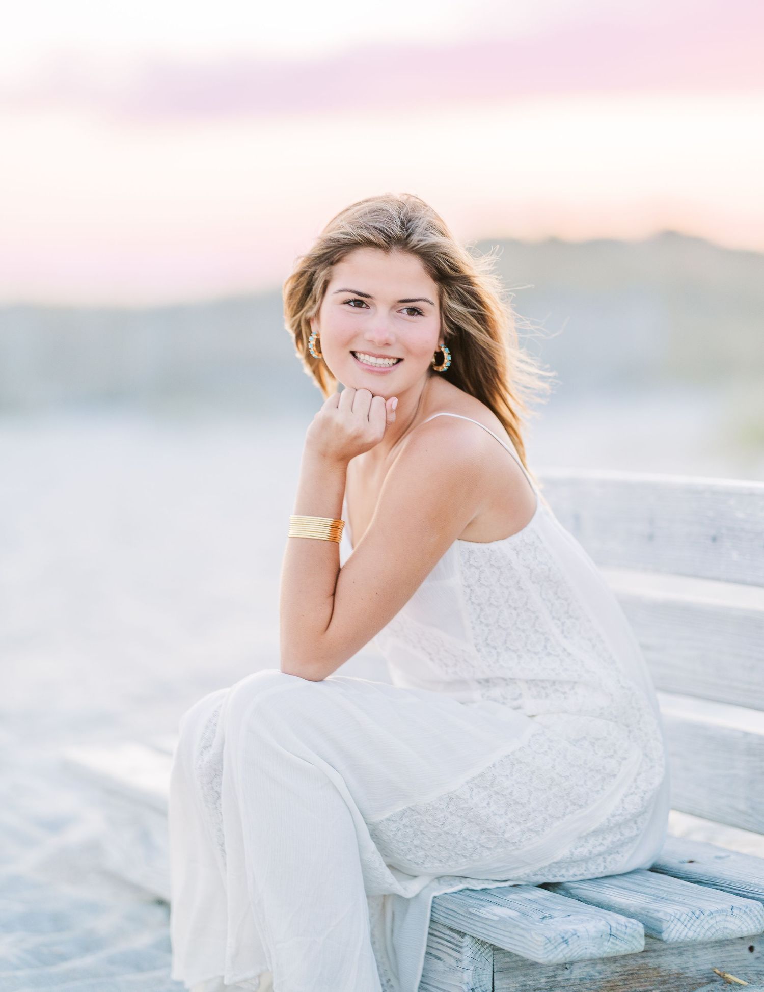 Elegant white dress photoshoot on a weathered wooden bench at the beach during sunset.