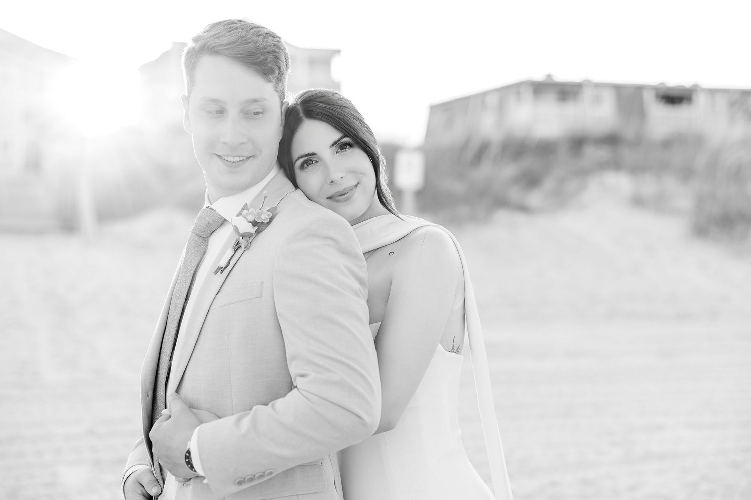 Black and white beach wedding photo of bride and groom embracing, with sunlight glowing behind them in Carolina Beach near Wilmington, NC.