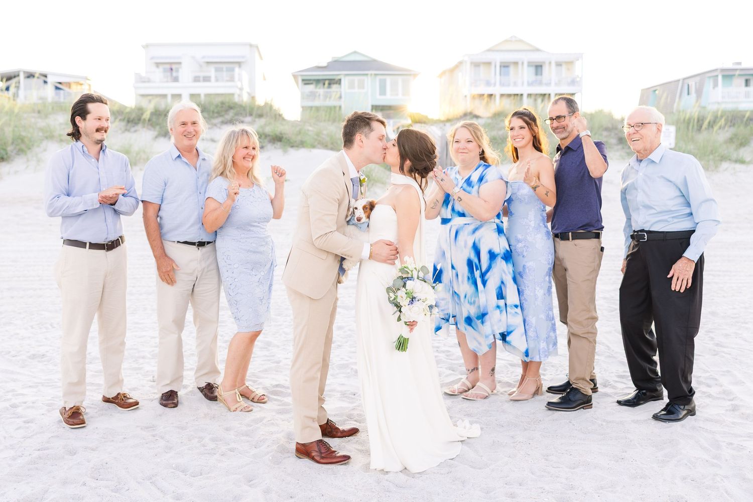 Newlyweds kiss surrounded by smiling family members on a sandy beach after their intimate wedding ceremony in Carolina Beach near Wilmington