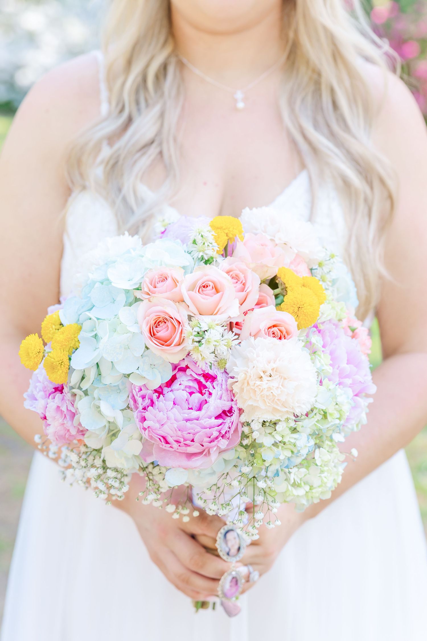 Bride holds vibrant wedding bouquet with pink peonies, roses, hydrangeas, and yellow flowers in white dress in Airlie Gardens in Wilmington,