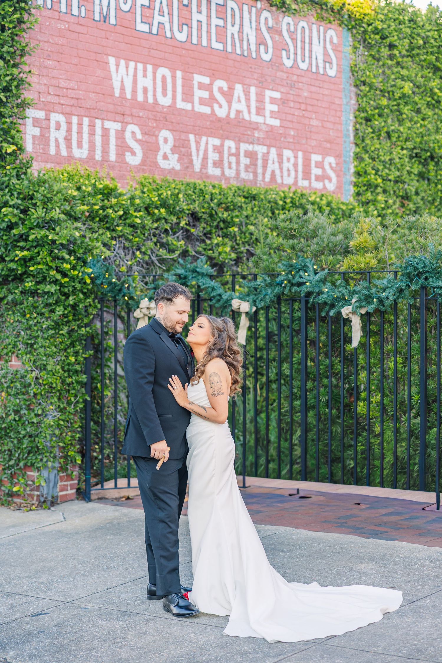 Romantic wedding portrait against vintage wholesale fruits and vegetables sign on brick wall.