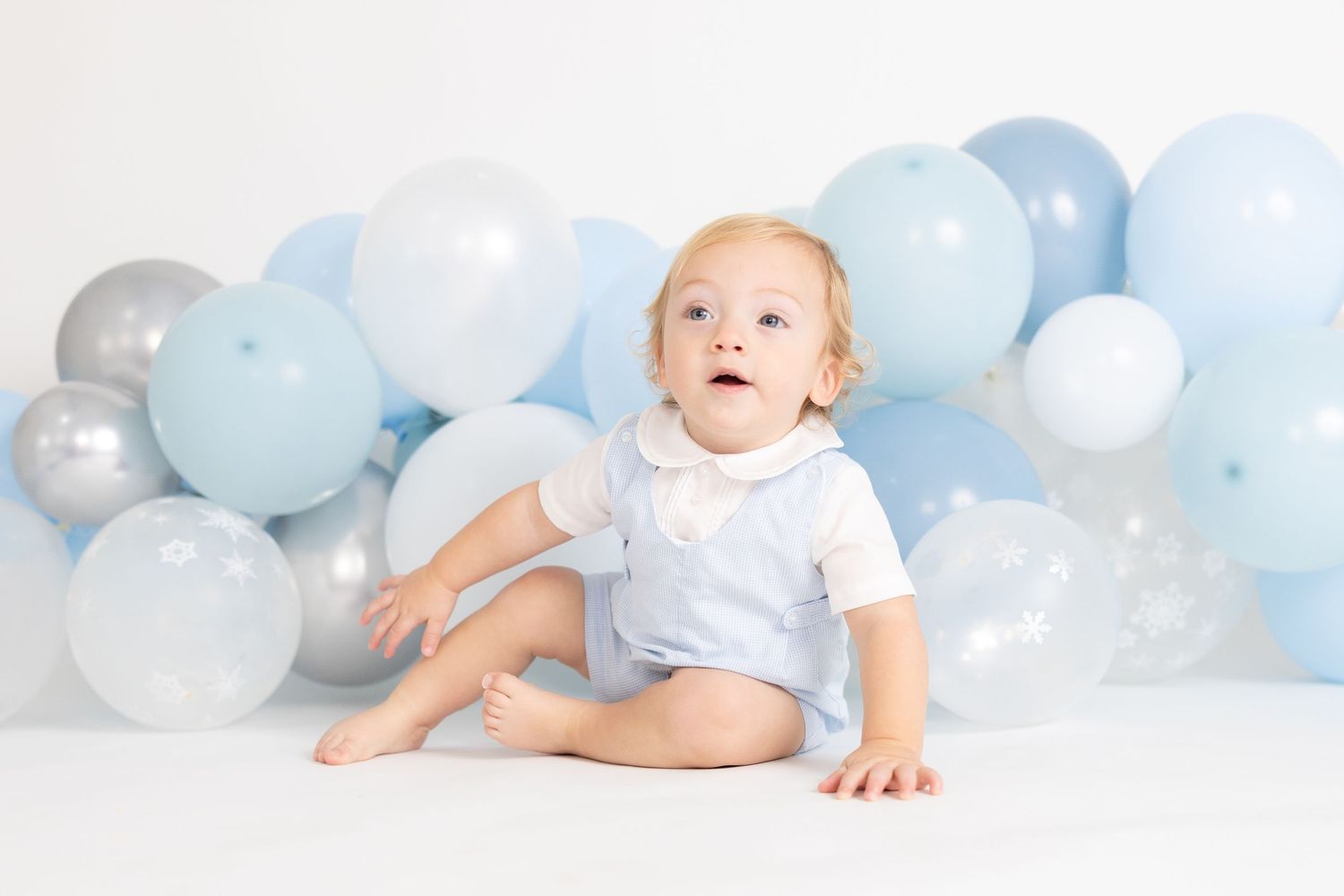 Baby lying on white floor with blue balloon garland decoration.