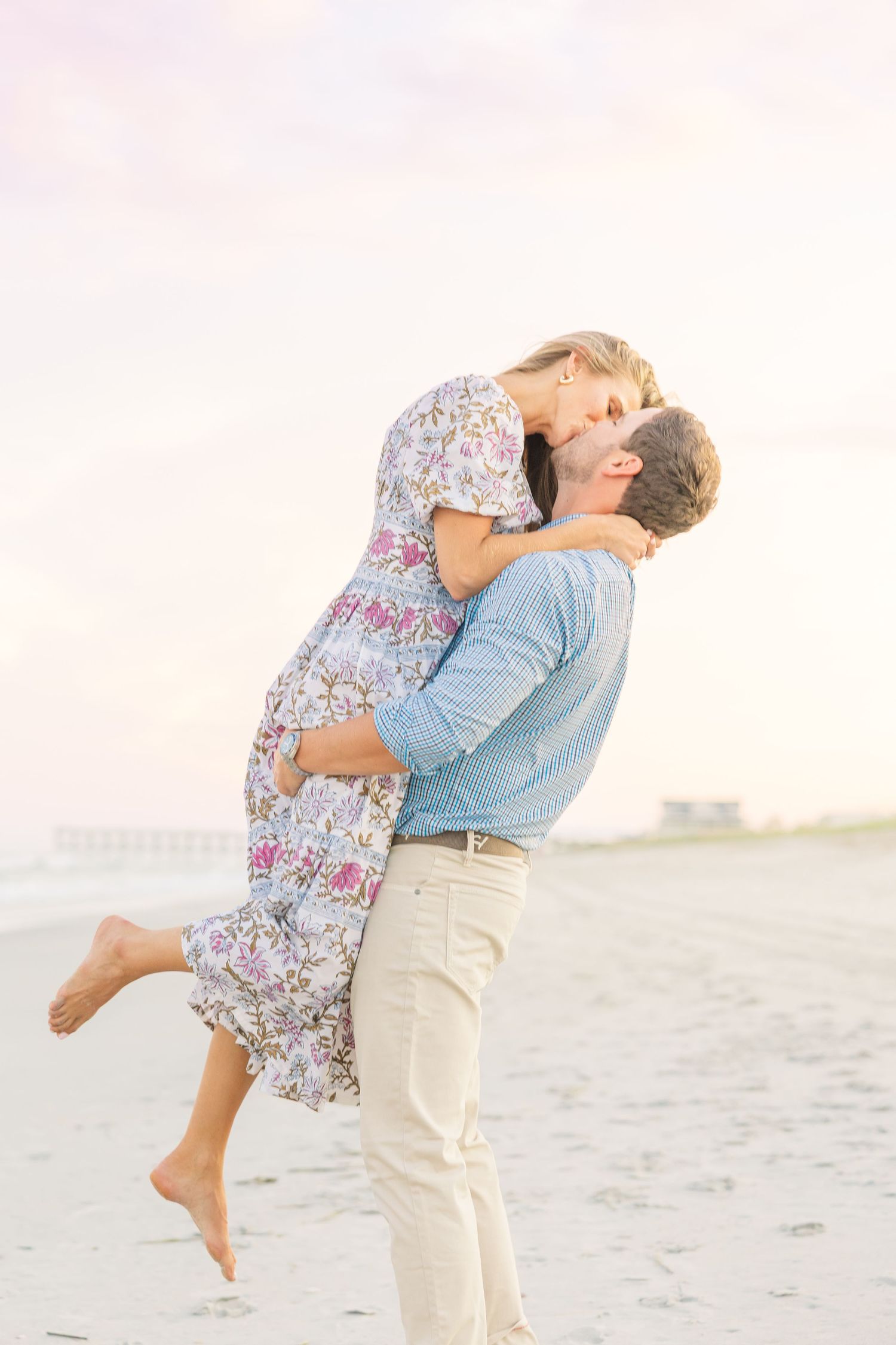 Romantic couple embracing on a sandy beach at sunset with one person lifted in the air.