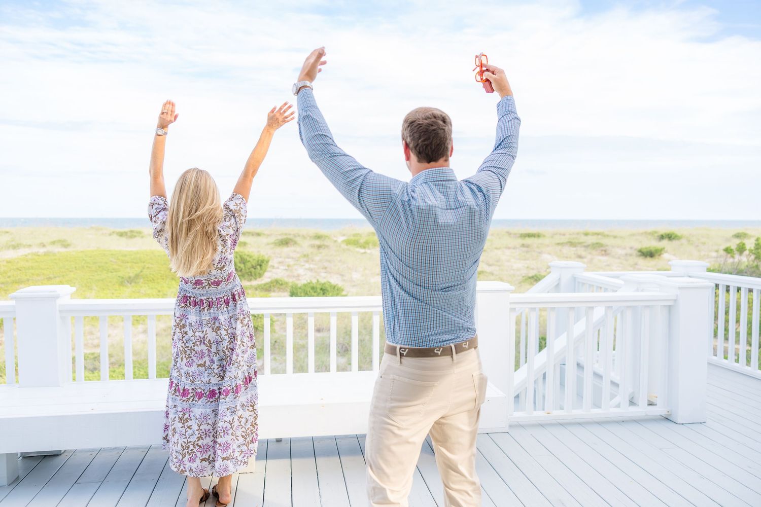 Joyful couple celebrating with raised arms on a beachfront deck.
