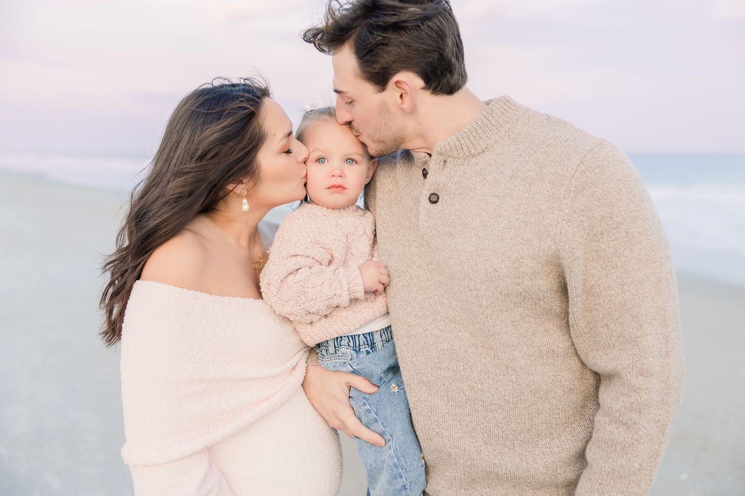 Family embraces in soft sweaters on a serene beach during sunset.