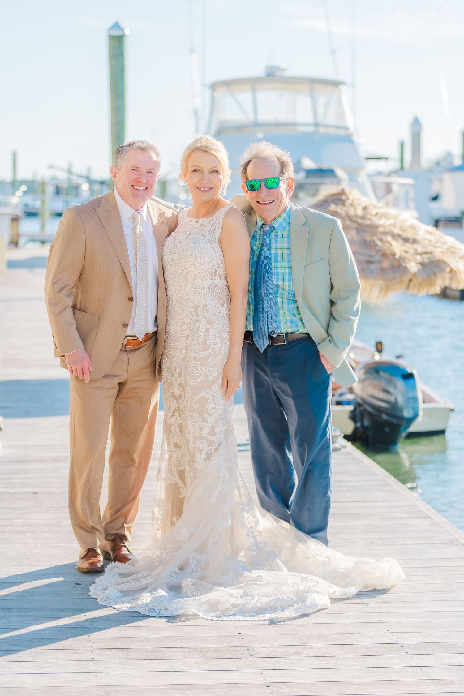 Wedding party poses together on a wooden dock with boats and marina in the background.