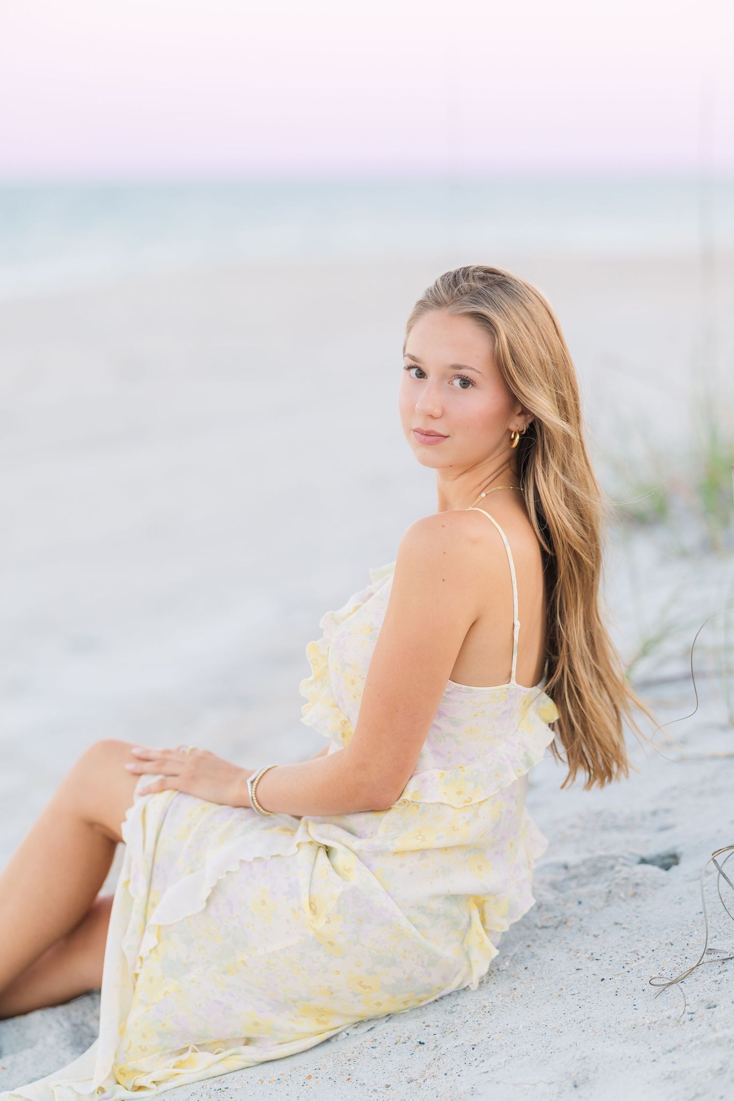 Summer beach portrait session featuring yellow floral dress on sandy shore.