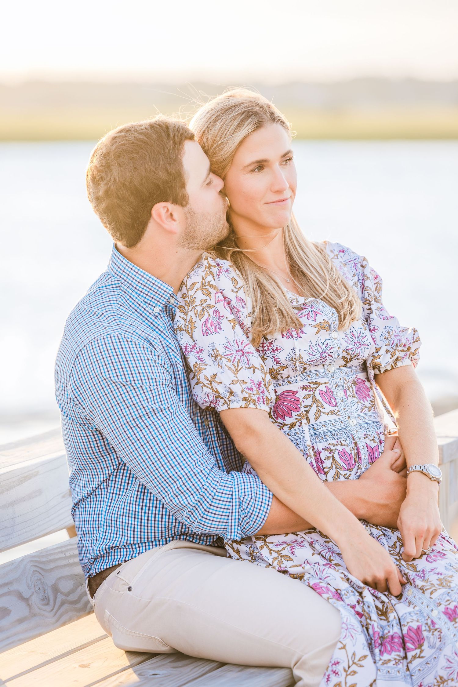 A couple in coordinated outfits sharing a tender moment by the water at golden hour.