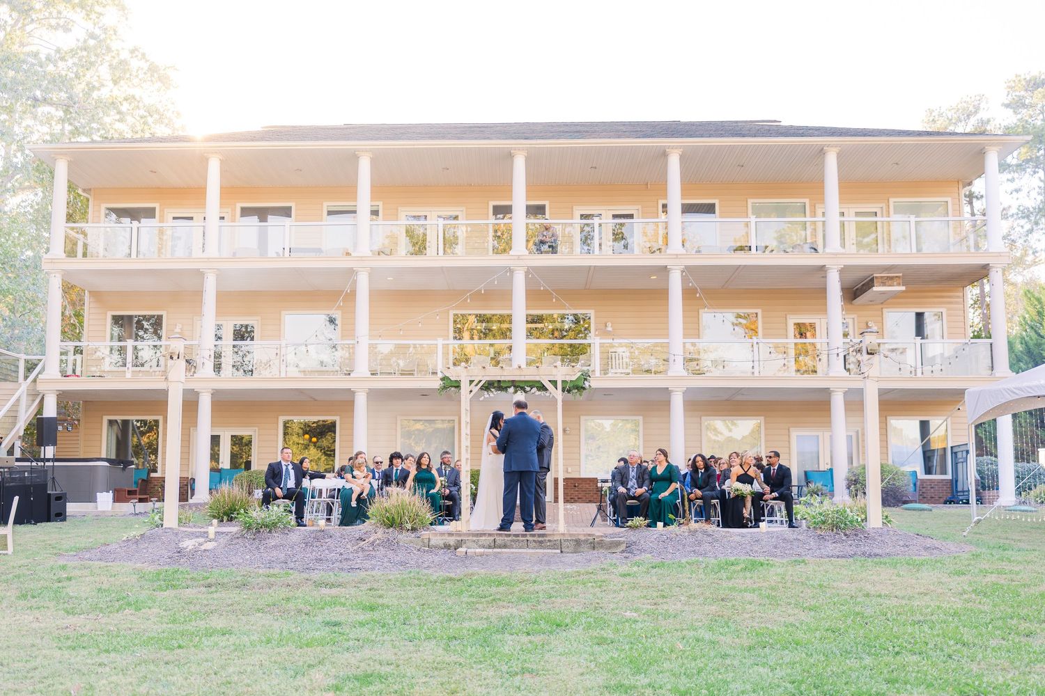 Panoramic view of a wedding venue with a covered porch and guests seated on the lawn wedding groom bride lake Gaston photographer light airy