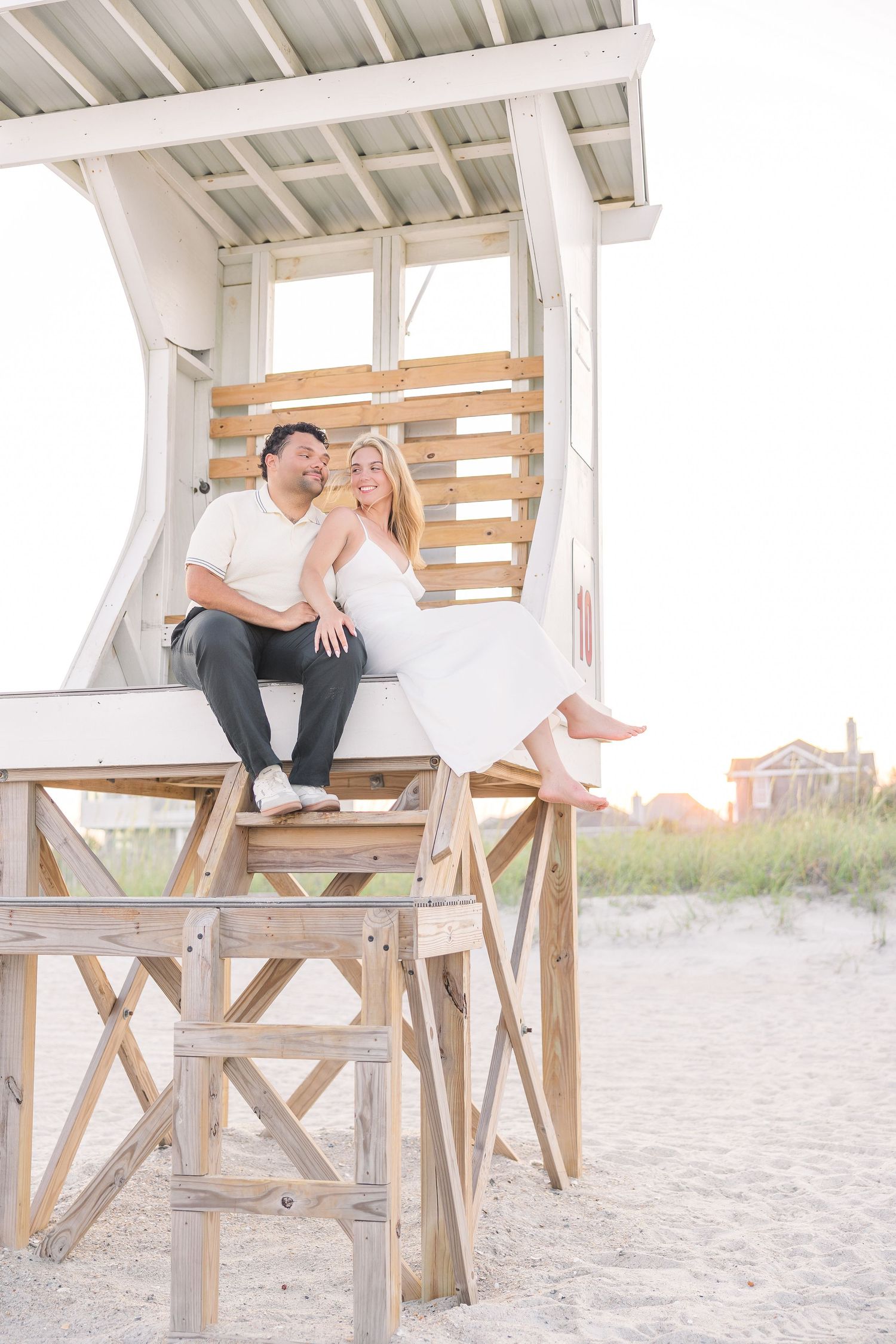 Couple relaxes together on a beachside lifeguard tower at golden hour on sandy shores.