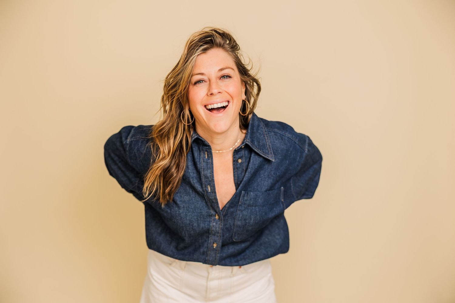 Energetic fashion poses in denim shirt against beige studio background.