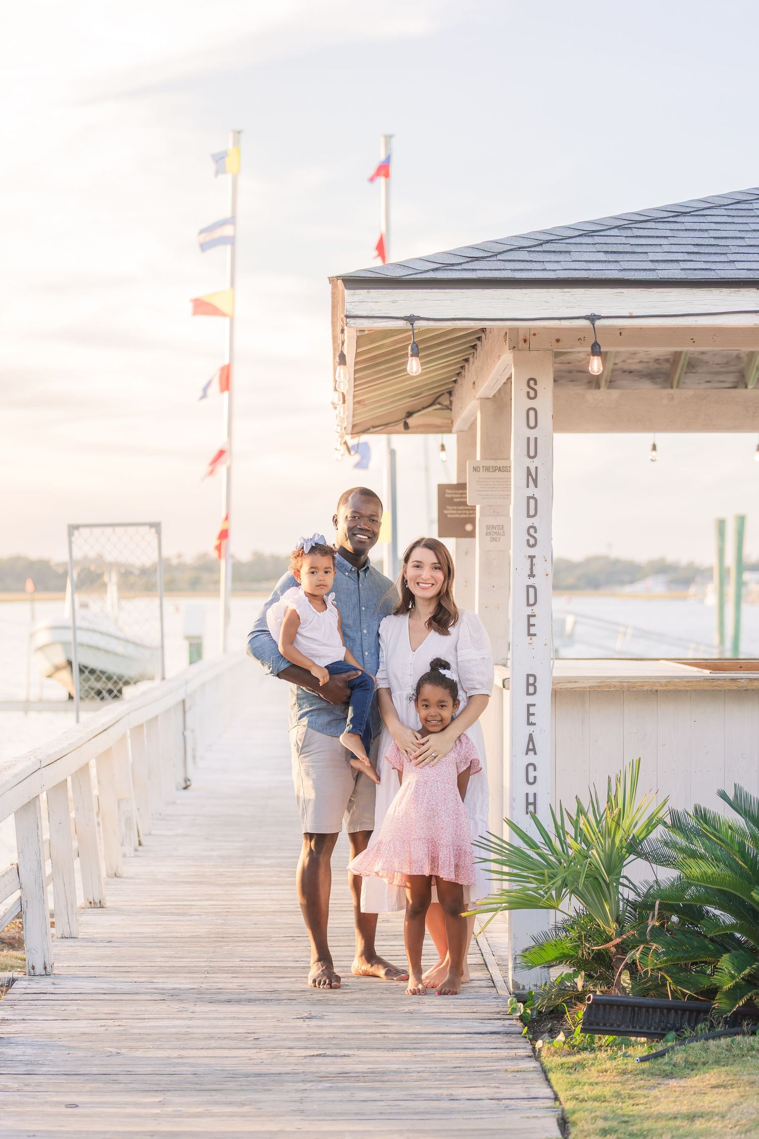 Family shares joyful moments on a coastal boardwalk with flags waving in background.