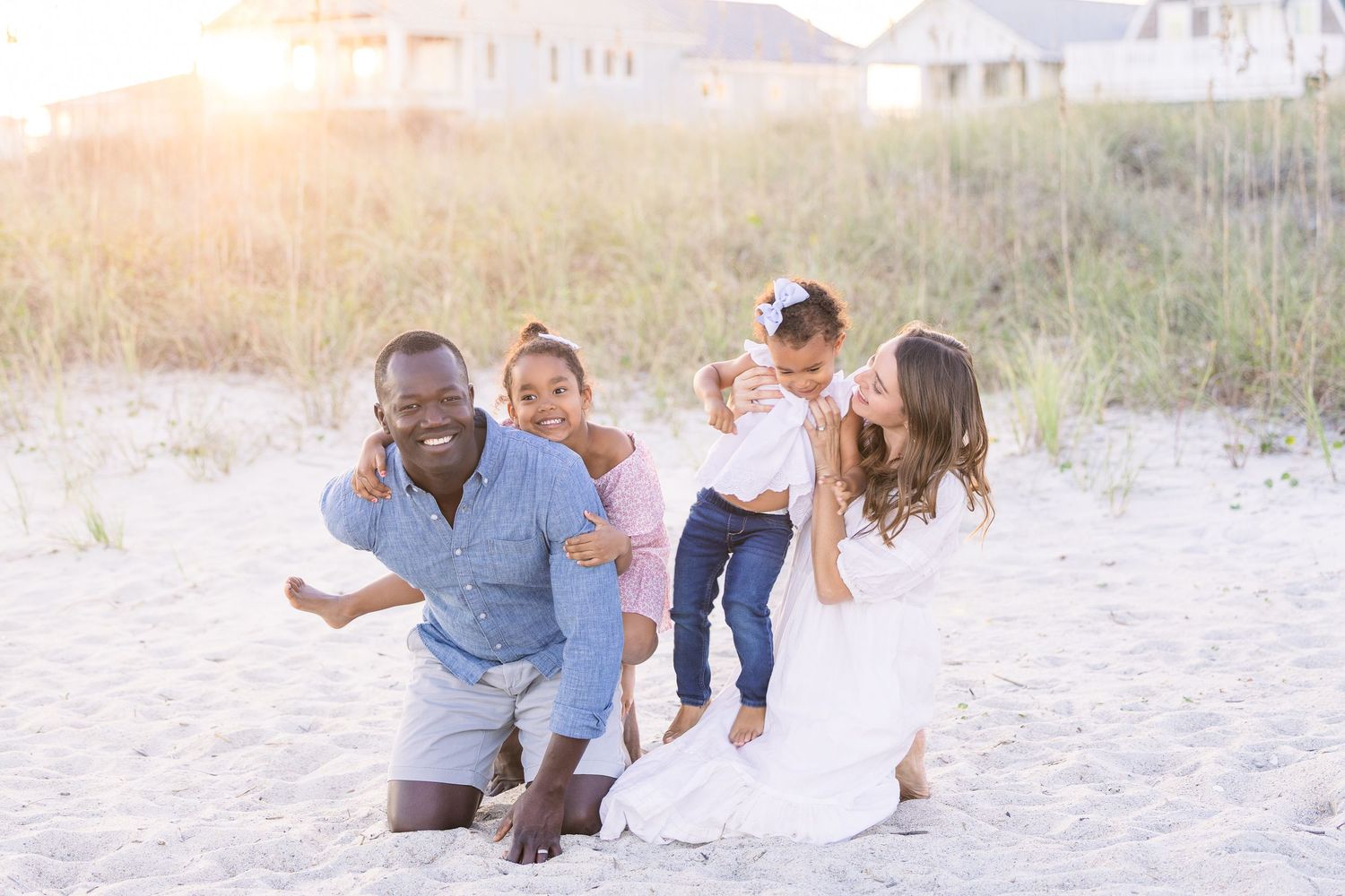 Family enjoying a playful moment together on a sandy beach at sunset.