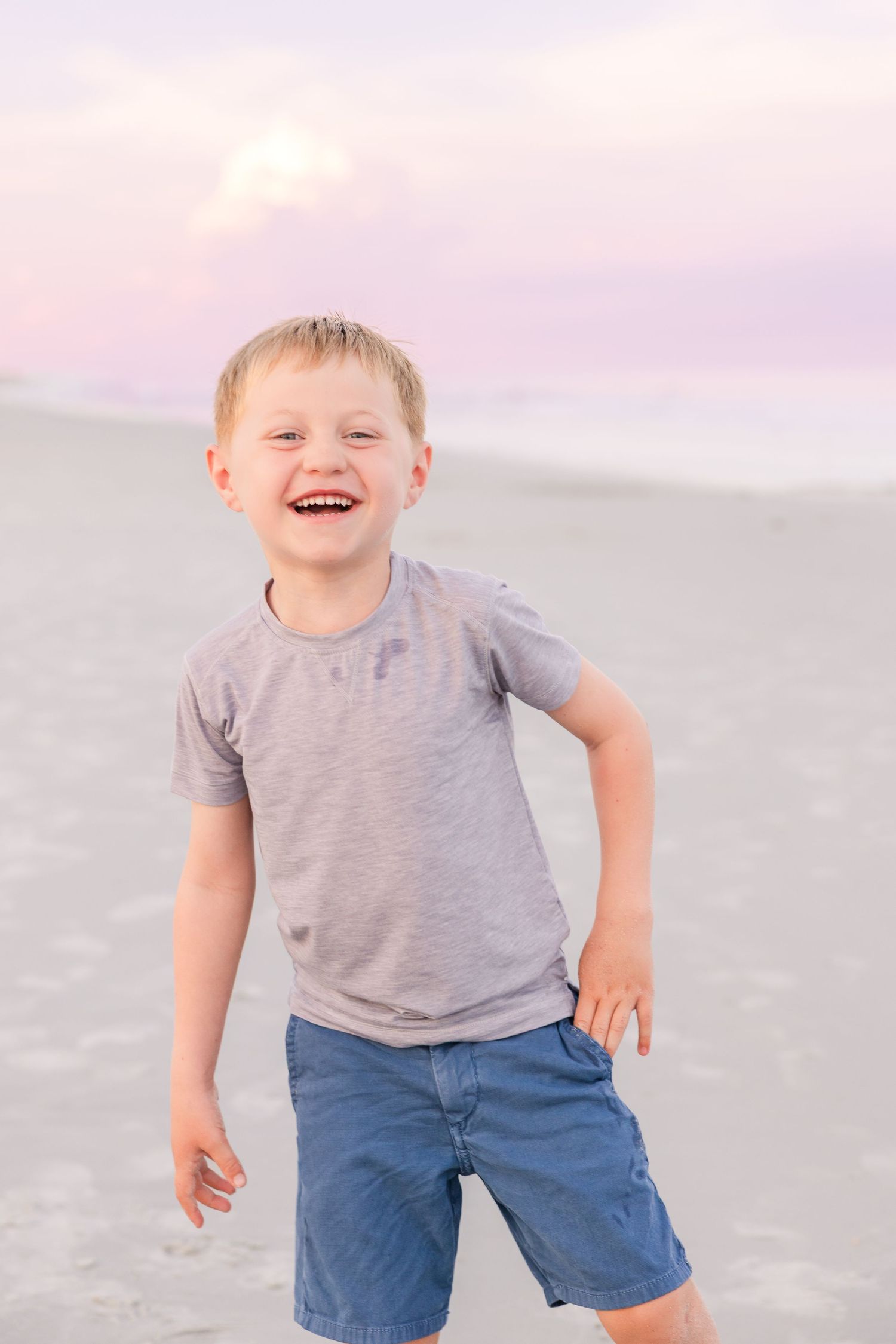 Playful child in grey shirt running and laughing on beach at dusk.