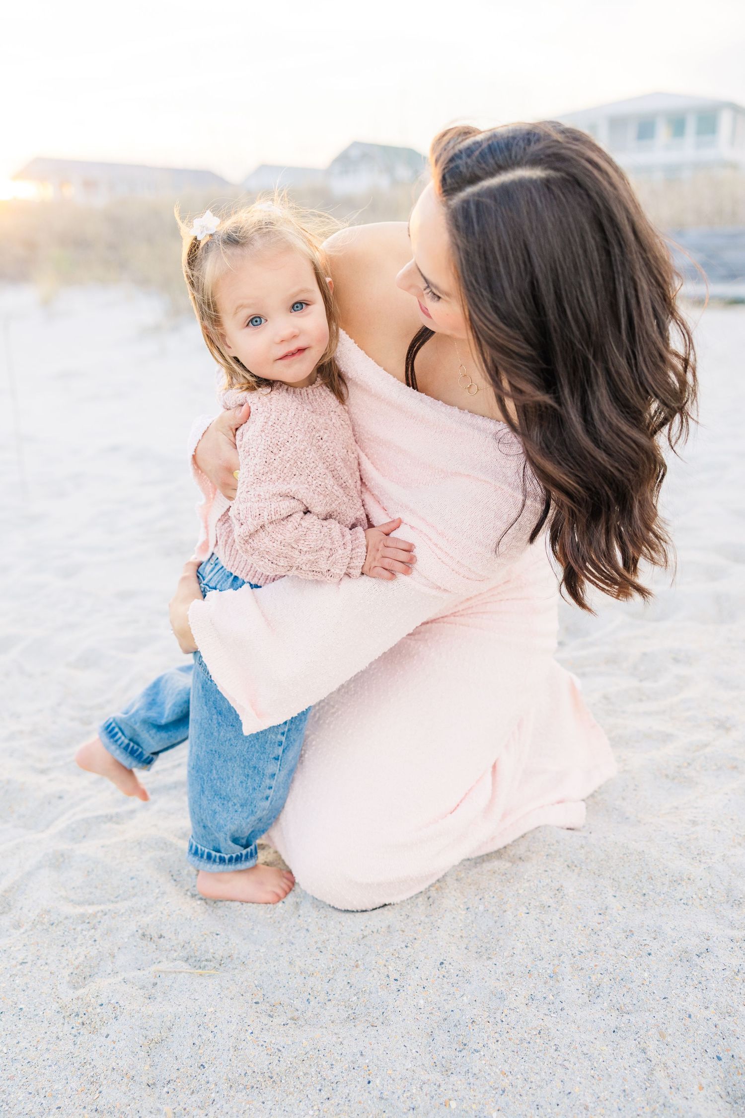 Playful beach photoshoot with parent and child in soft pink attire.
