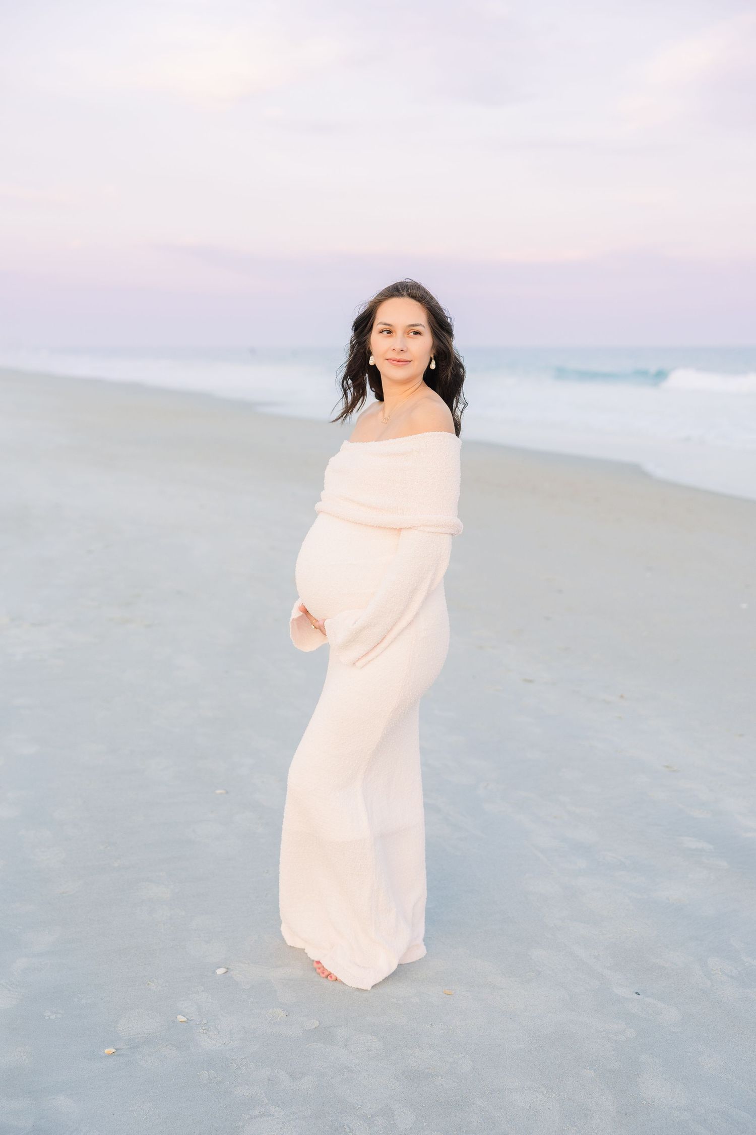 Woman in flowing cream dress dances on beach during golden hour.