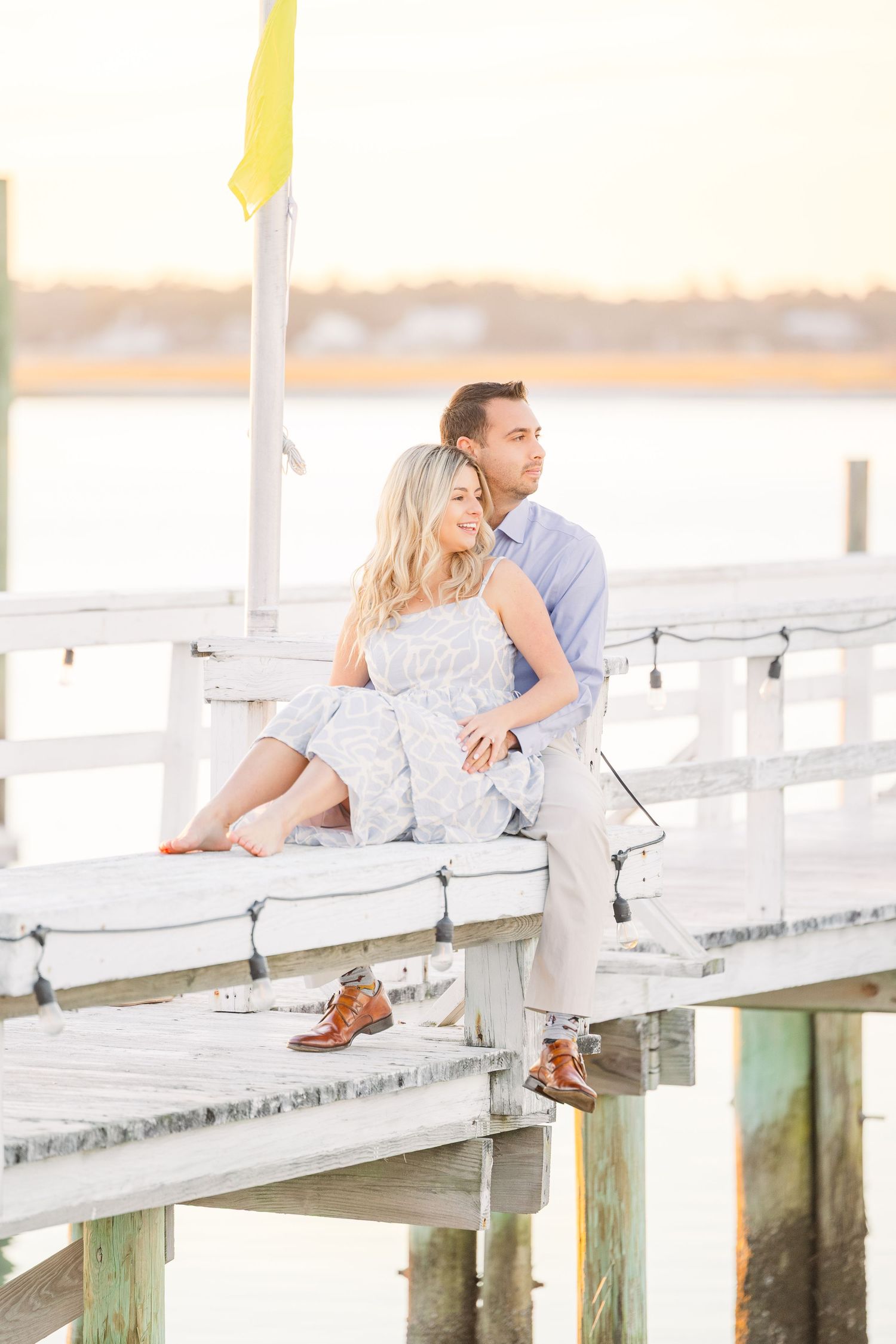 Relaxed couple lounging on coastal pier with dangling feet and yellow flag above.