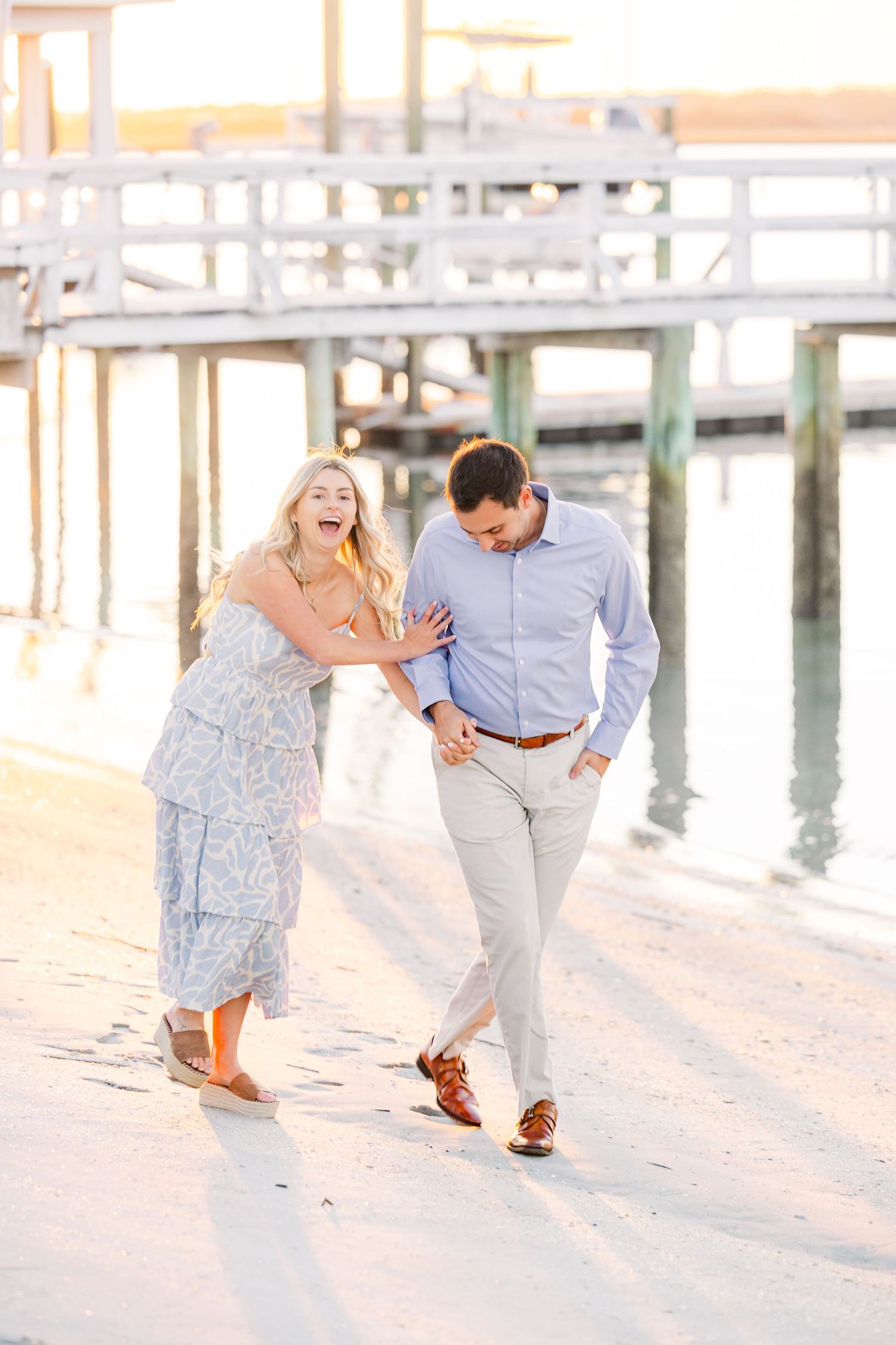 Joyful moment captured of couple laughing while walking along waterfront pier.