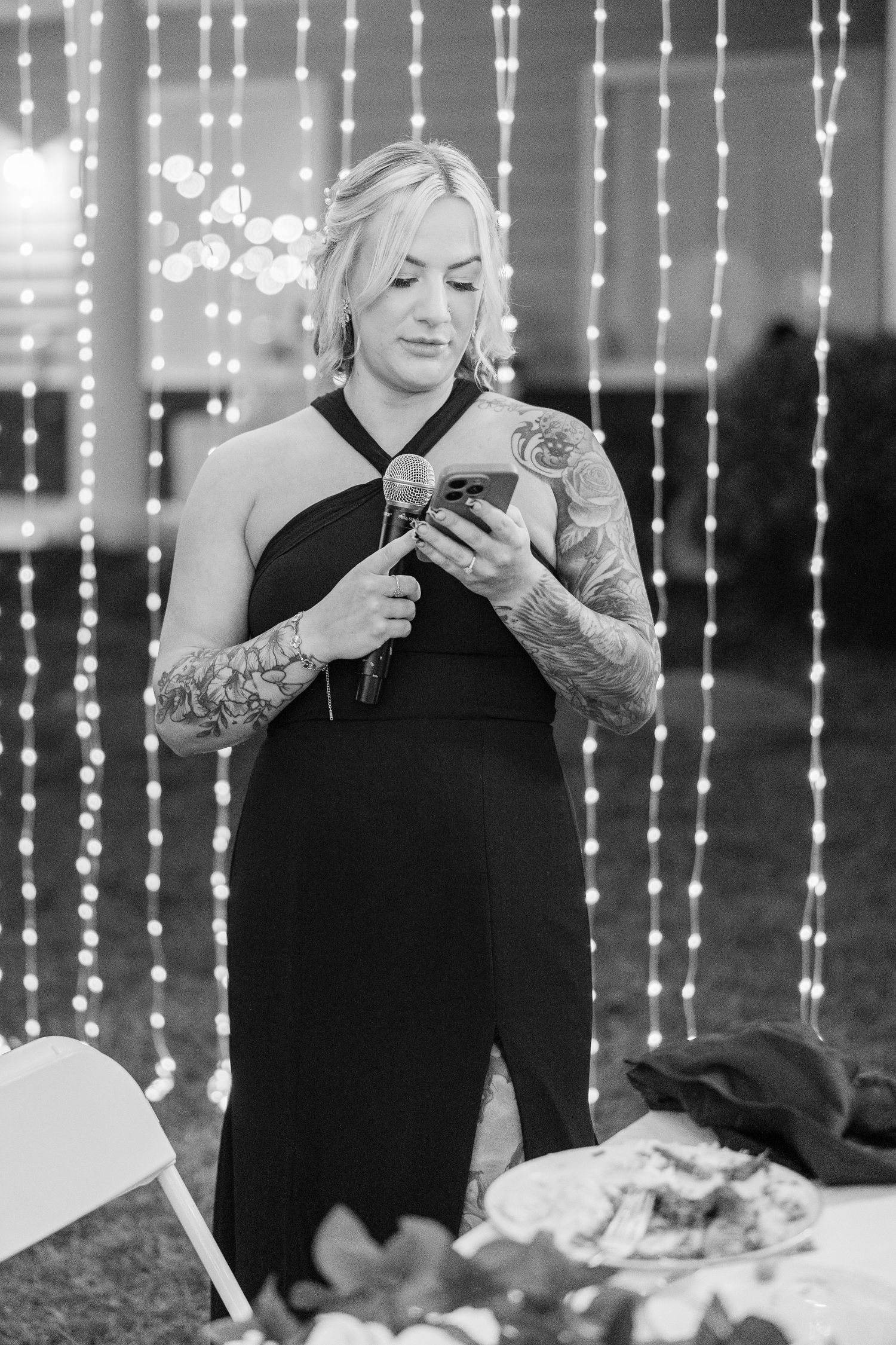 Black and white photo of guests using phones under hanging string lights at reception wedding groom bride lake Gaston photographer light air