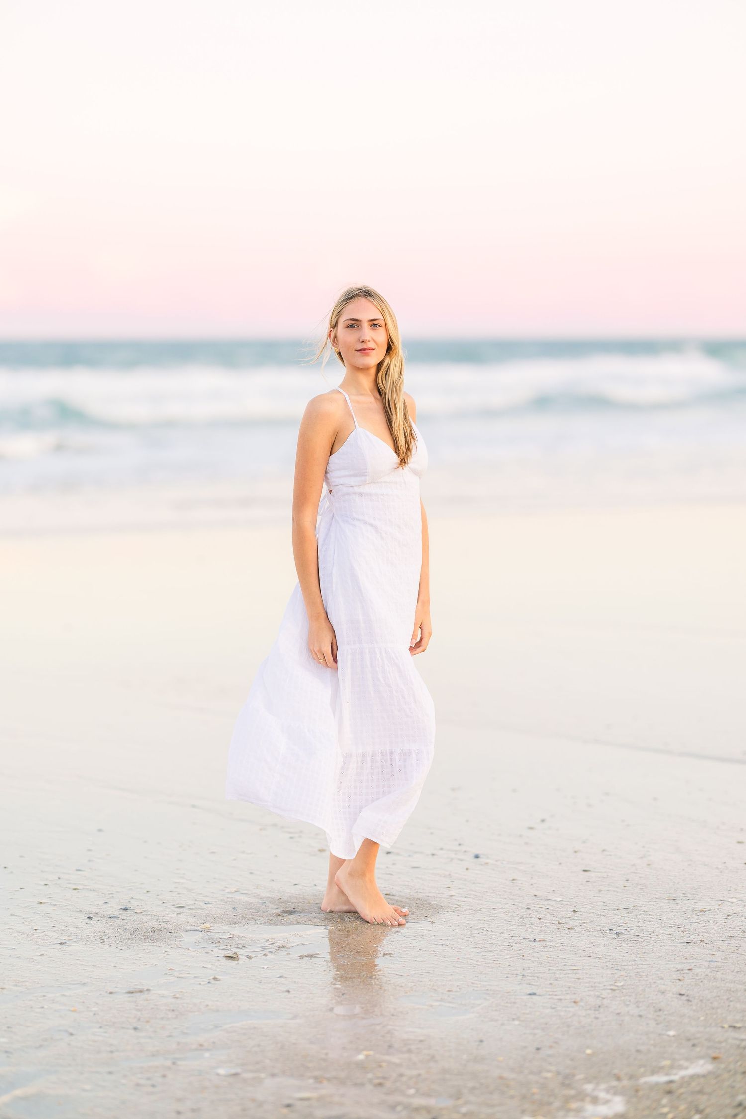 Barefoot beach portrait in white maxi dress during pastel sunset.