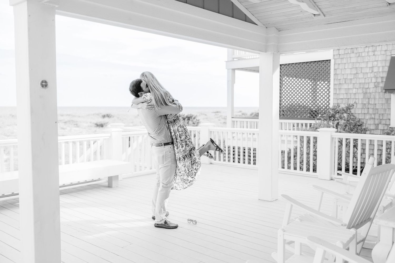 Black and white photo of a couple dancing playfully on a seaside porch.