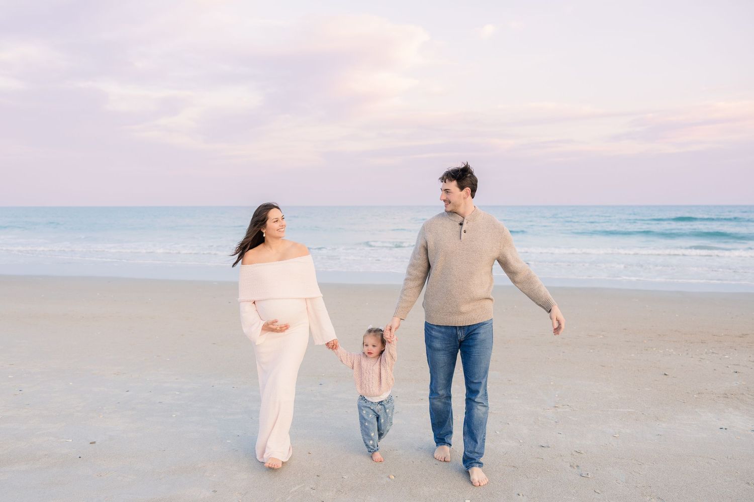 Family walking hand in hand along the shoreline at dusk.