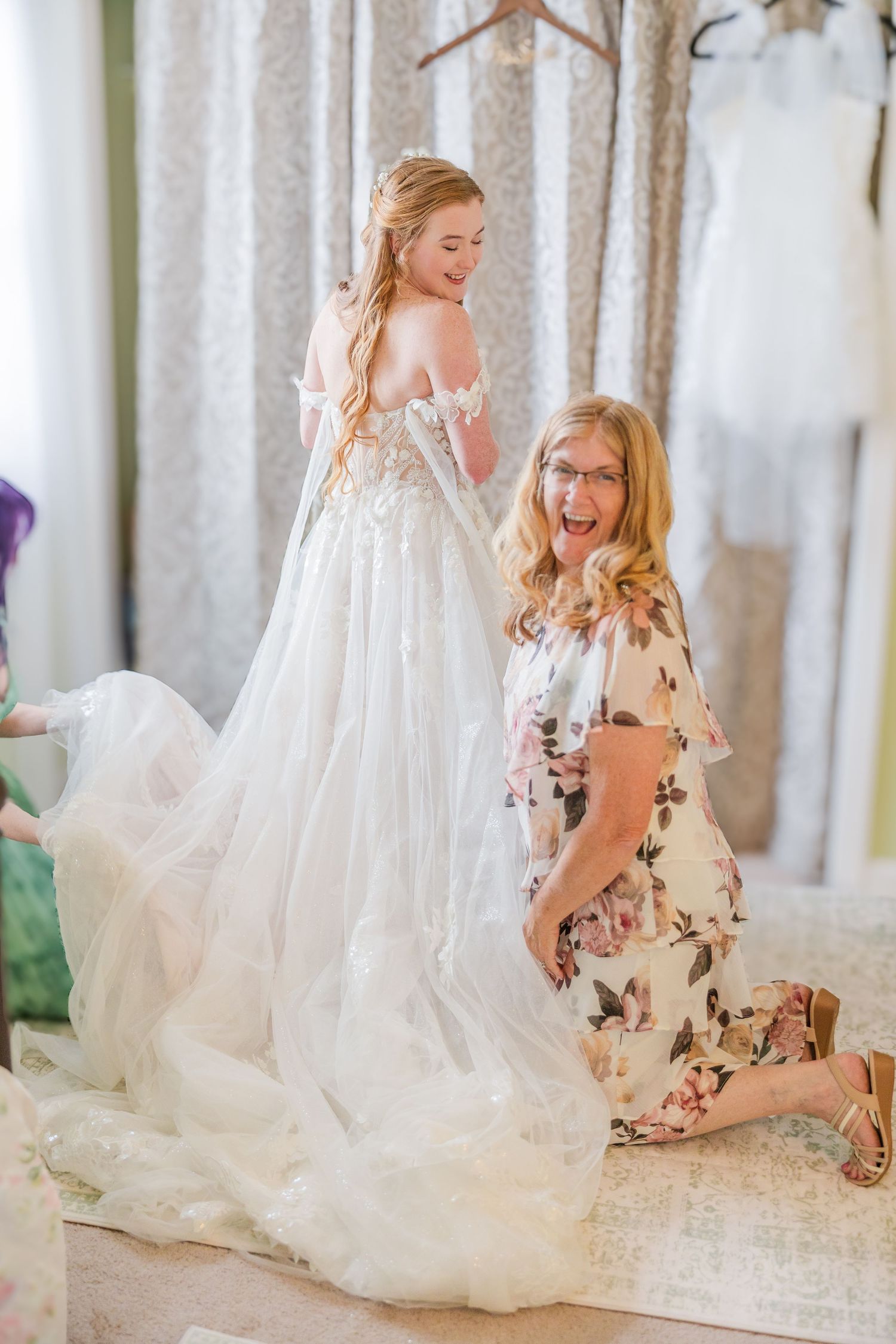 A bride trying on a flowing white wedding dress in a bridal boutique with floral curtains in a backyard wedding in wilmington, nc