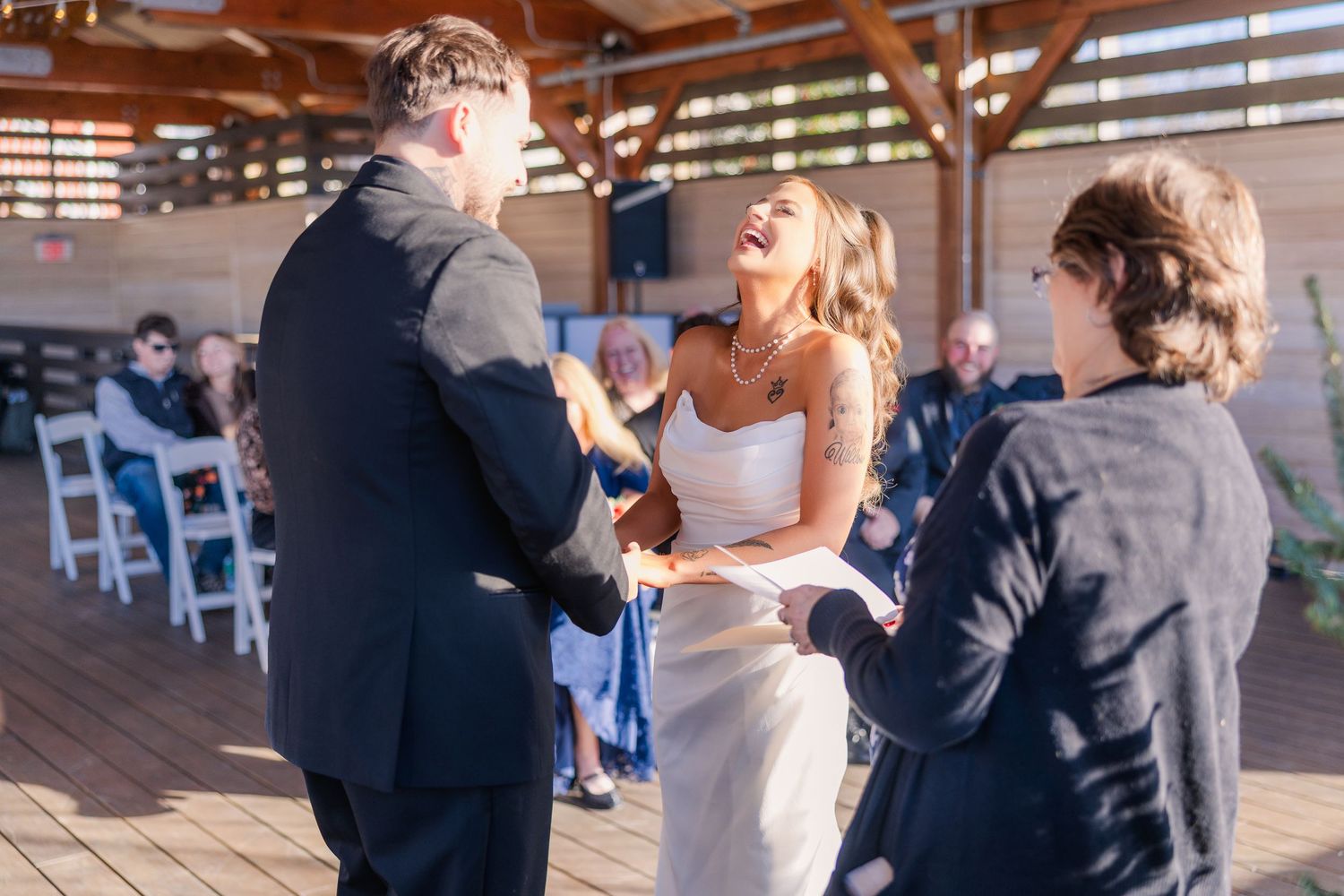 Intimate wedding ceremony moment on a covered wooden deck with guests seated in background.