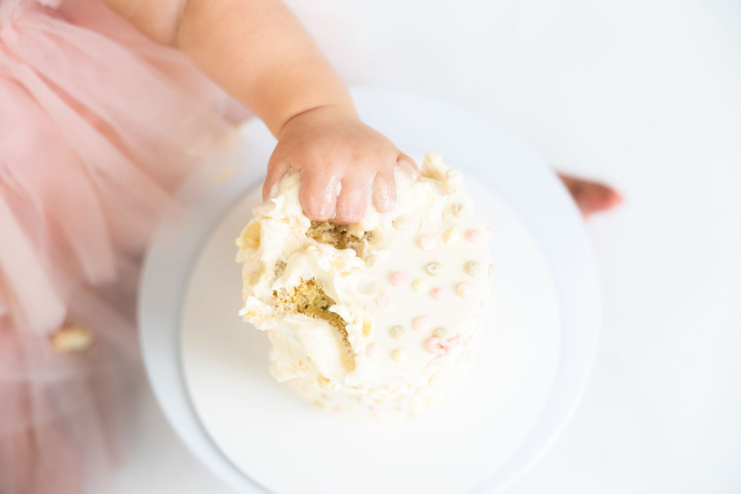 Close up of small hands touching white frosted cake on stand.