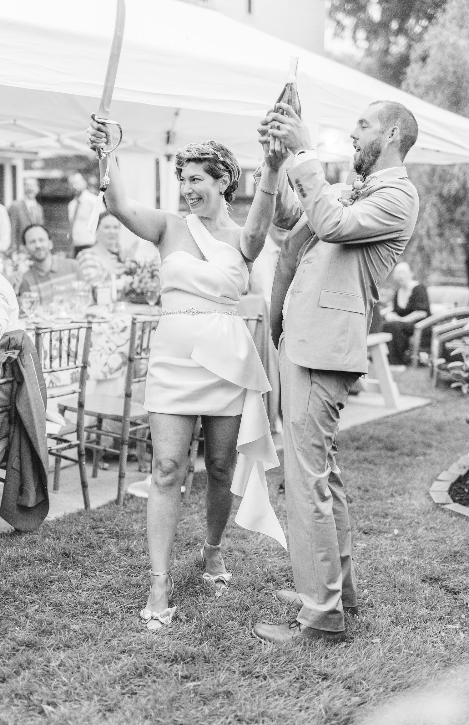 Wedding celebration scene with guests celebrating under outdoor tent in black and white.
