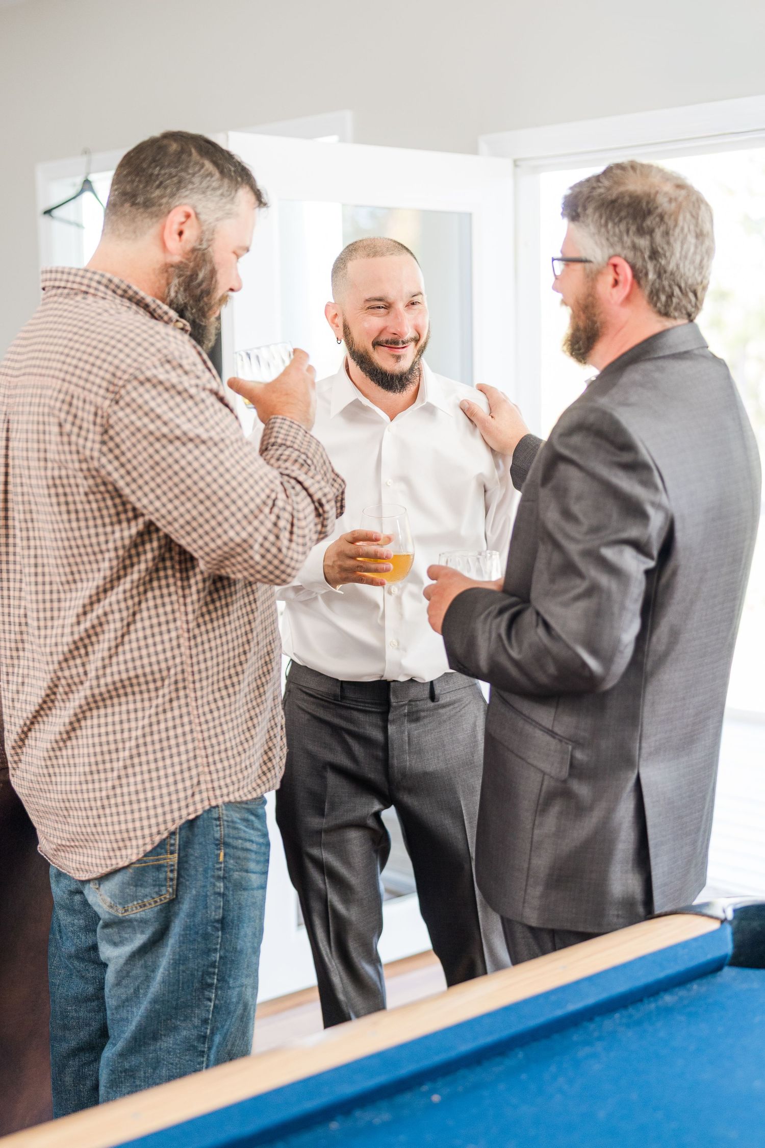 Friends gather around a blue pool table, sharing drinks and laughter at a casual event wedding groom bride lake Gaston photographer light ai