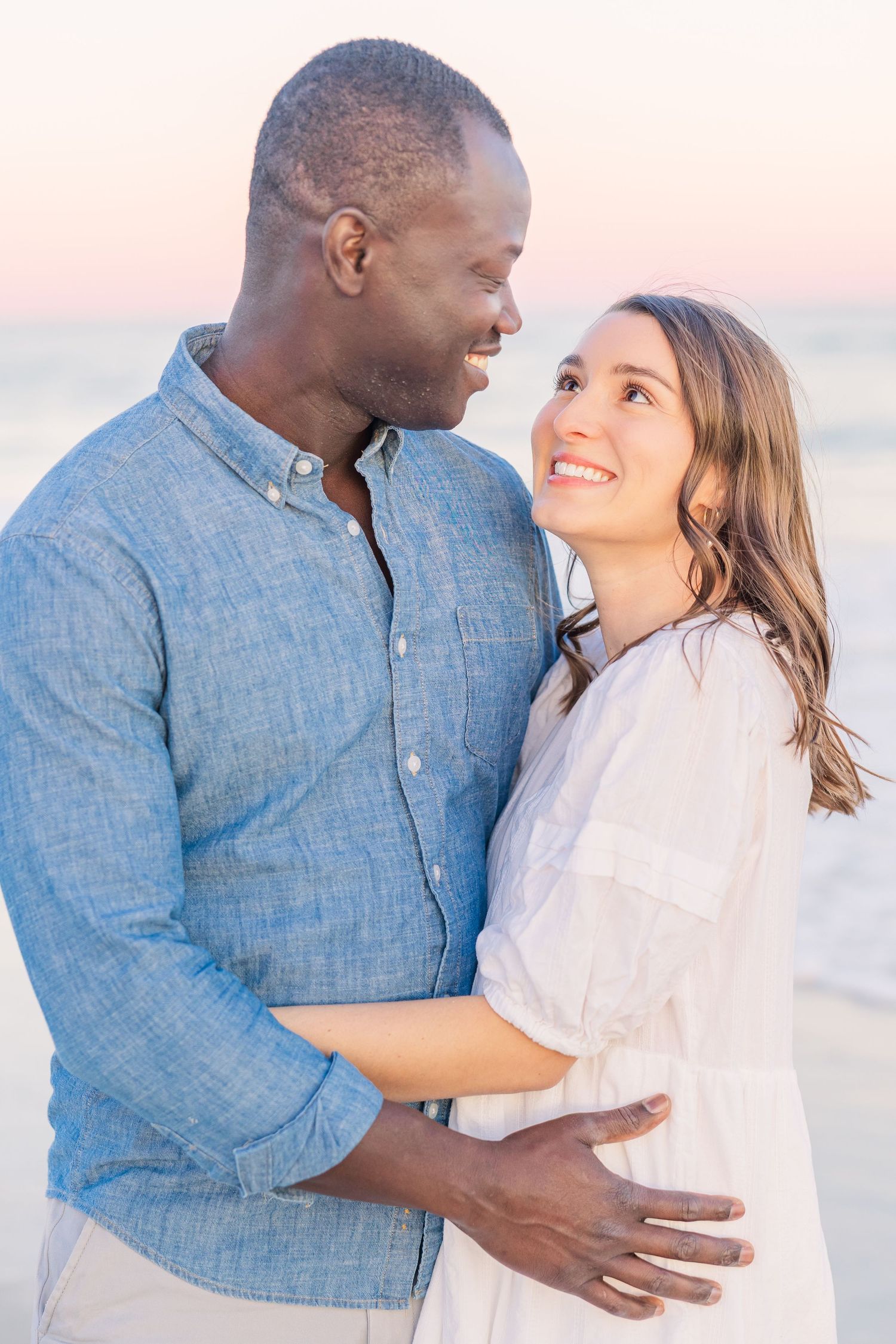 Romantic couple sharing intimate moments on beach during sunset wearing coordinated blue and white outfits.