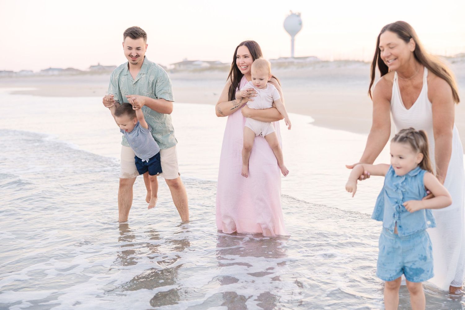 Family enjoying a playful moment together on a beach at sunset with gentle waves around them.