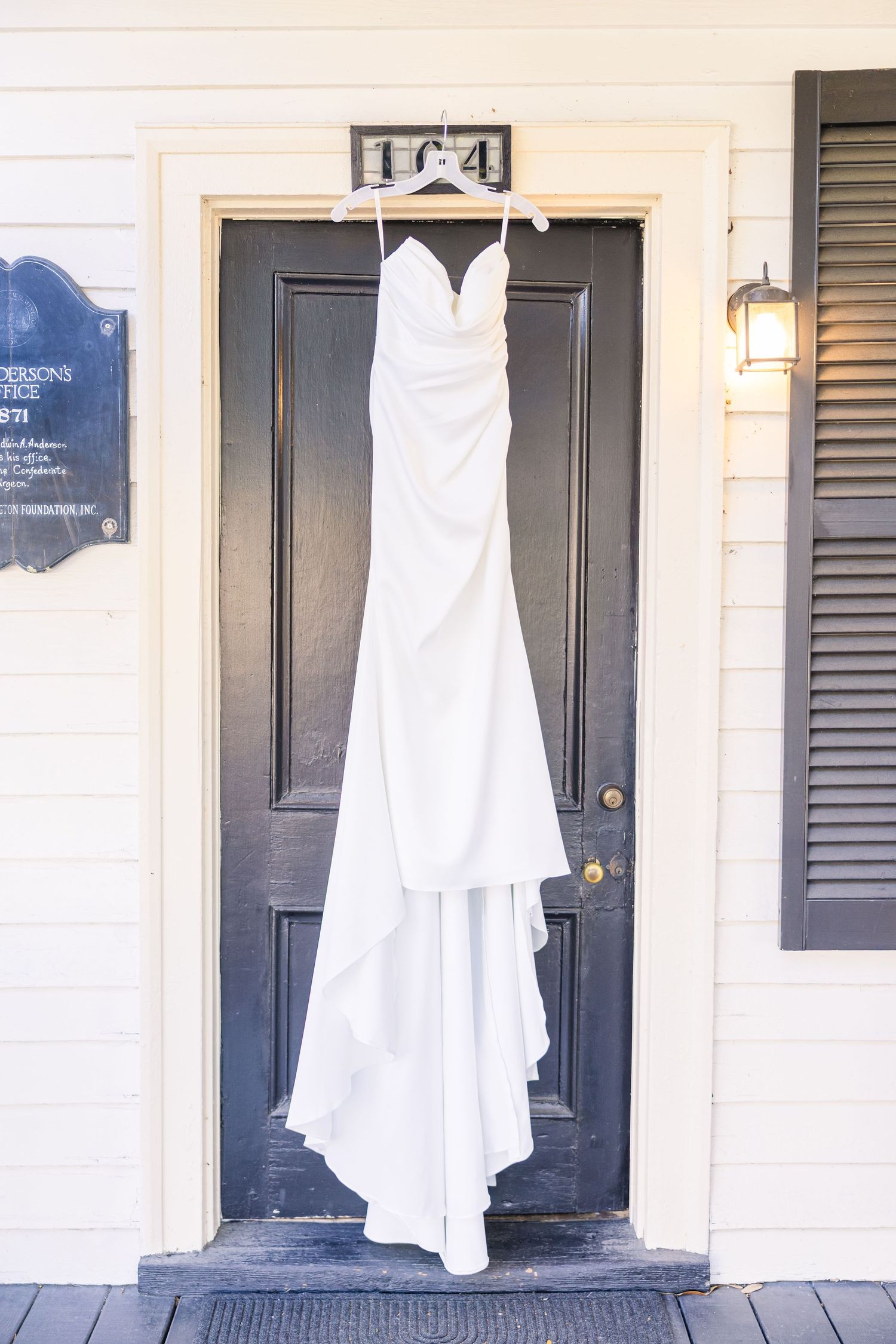 Elegant white wedding dress hanging on a black door with a house number 104 visible above.