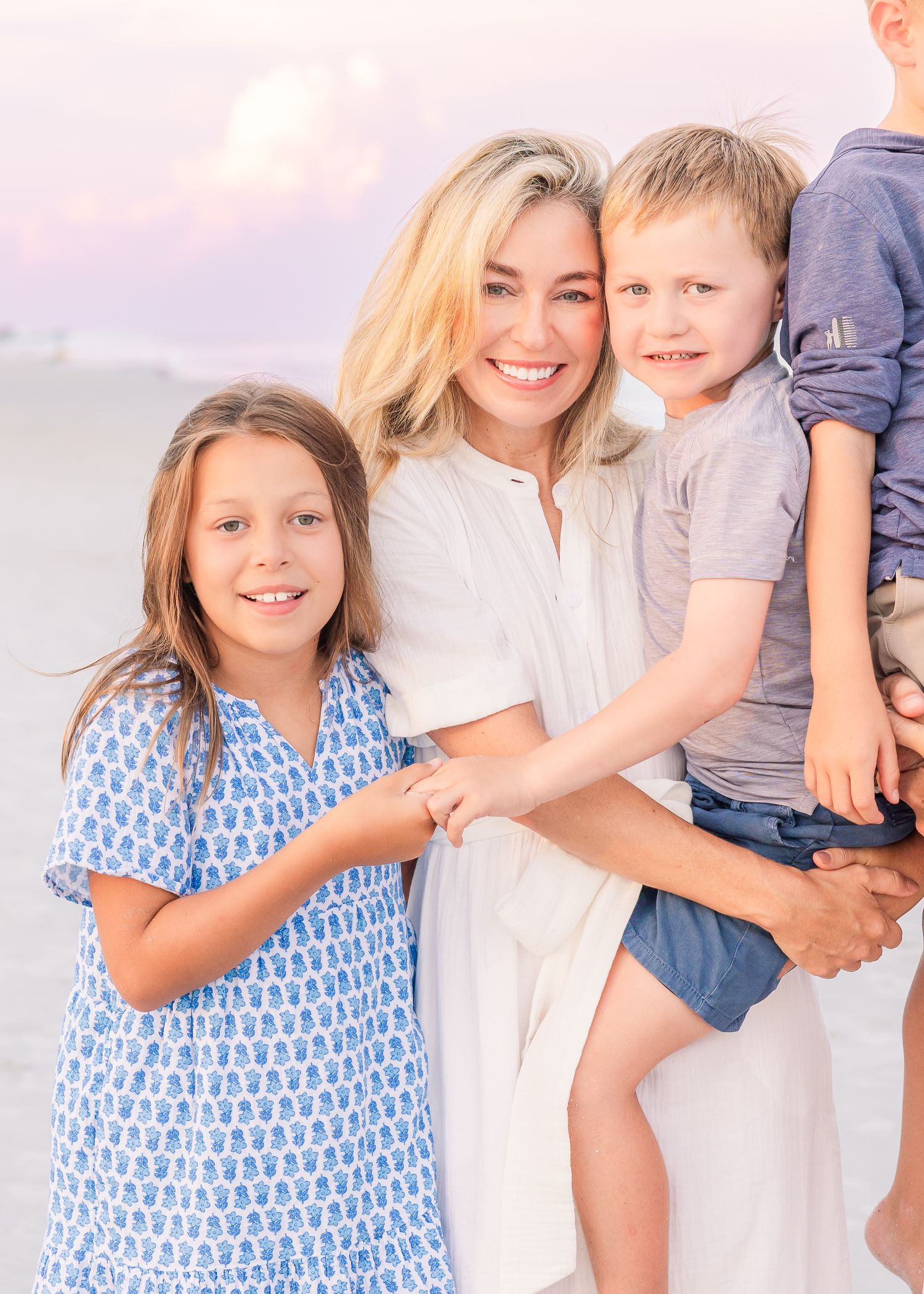 Close-up family portrait on beach with soft purple sunset sky.