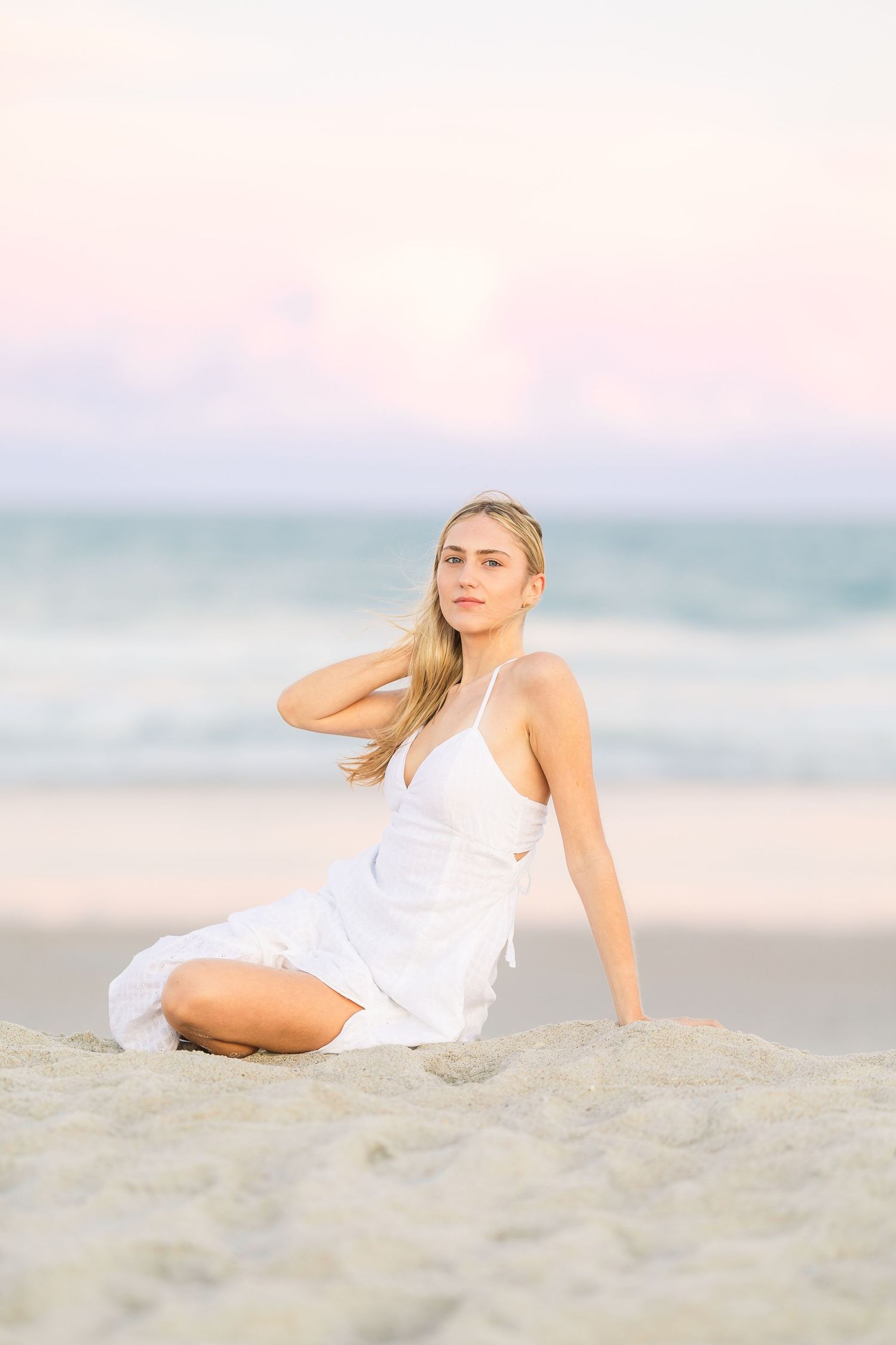 Artistic beach photography with model lounging on sand at sunset.
