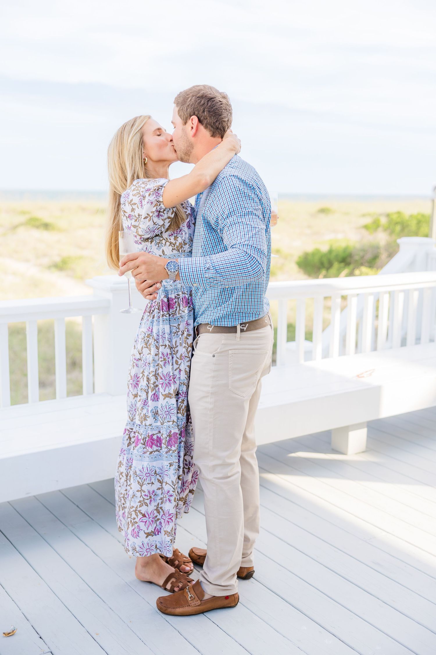 A romantic embrace between a couple on a coastal deck wearing coordinated blue and floral outfits.