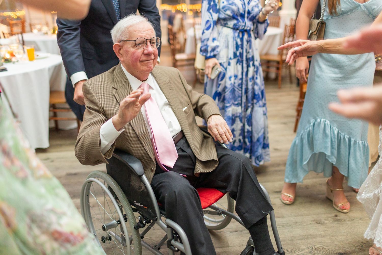 An elderly guest in a wheelchair smiles while participating in wedding festivities.