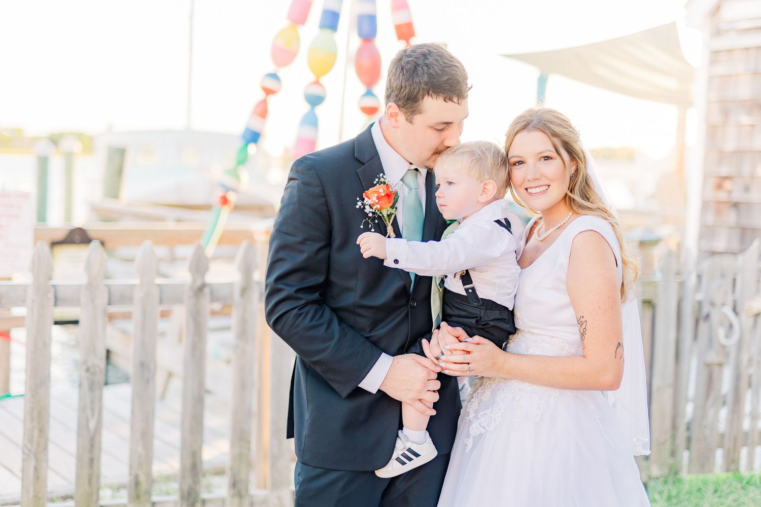 A couple shares a joyful moment with their baby at an outdoor wedding celebration.