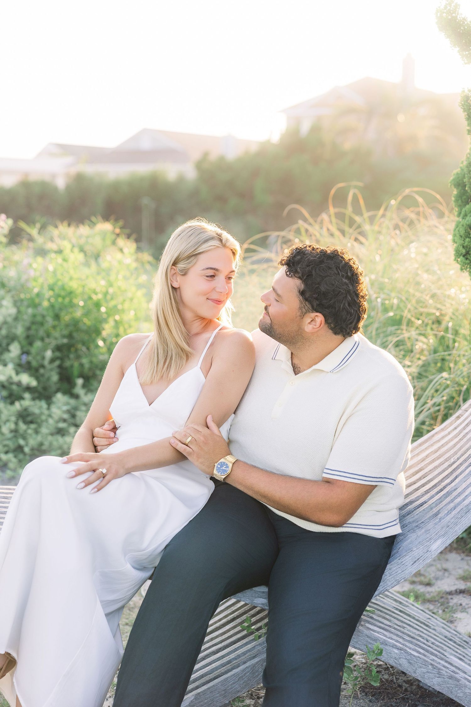 Couple sharing a romantic moment on a bench surrounded by lush greenery in golden hour light.