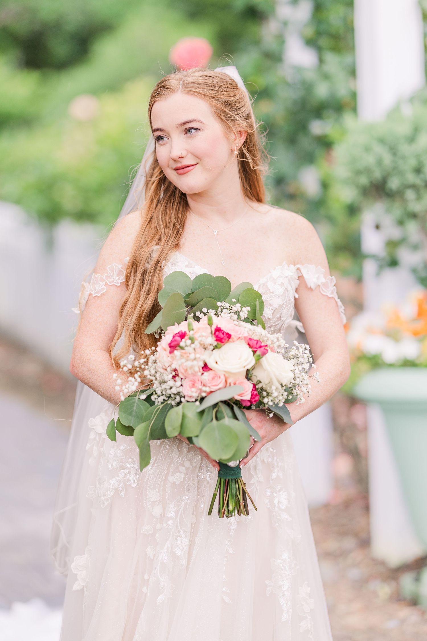 Bride in a flowing white dress holding a pink and white floral bouquet in an outdoor garden setting in harbor way gardens in Wrightsville